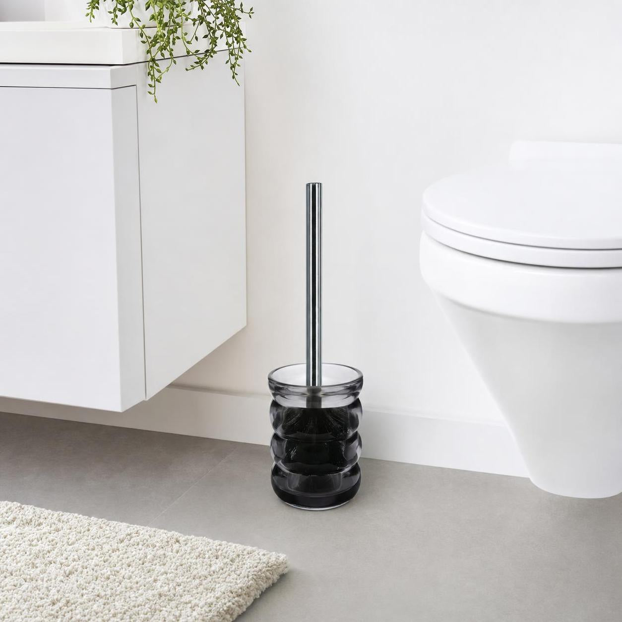 Eine schwarze WC-Bürste steht neben der Toilette im hellen Bad.