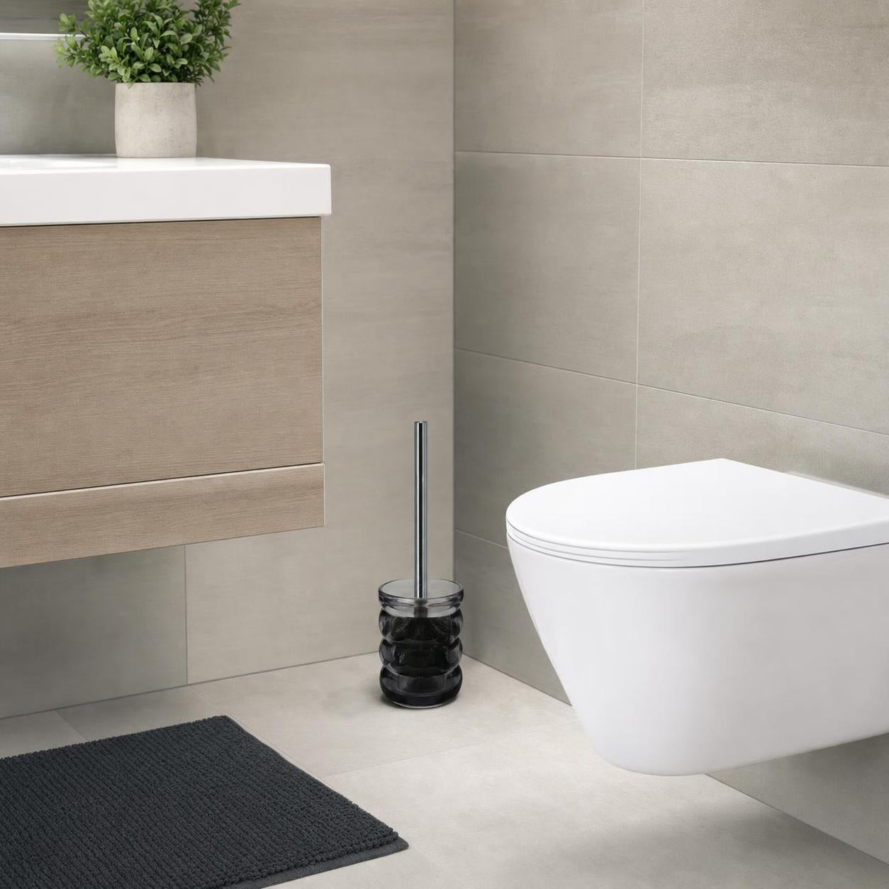 Eine WC-Bürste mit schwarzem Halter steht neben der Toilette.