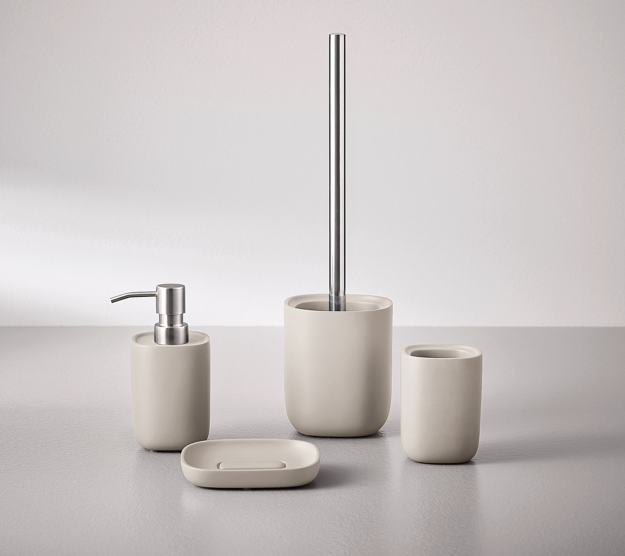 WC-Bürsten-Halter ALITA seidenfarben mit passendem Bad-Set auf grauer Fläche arrangiert.