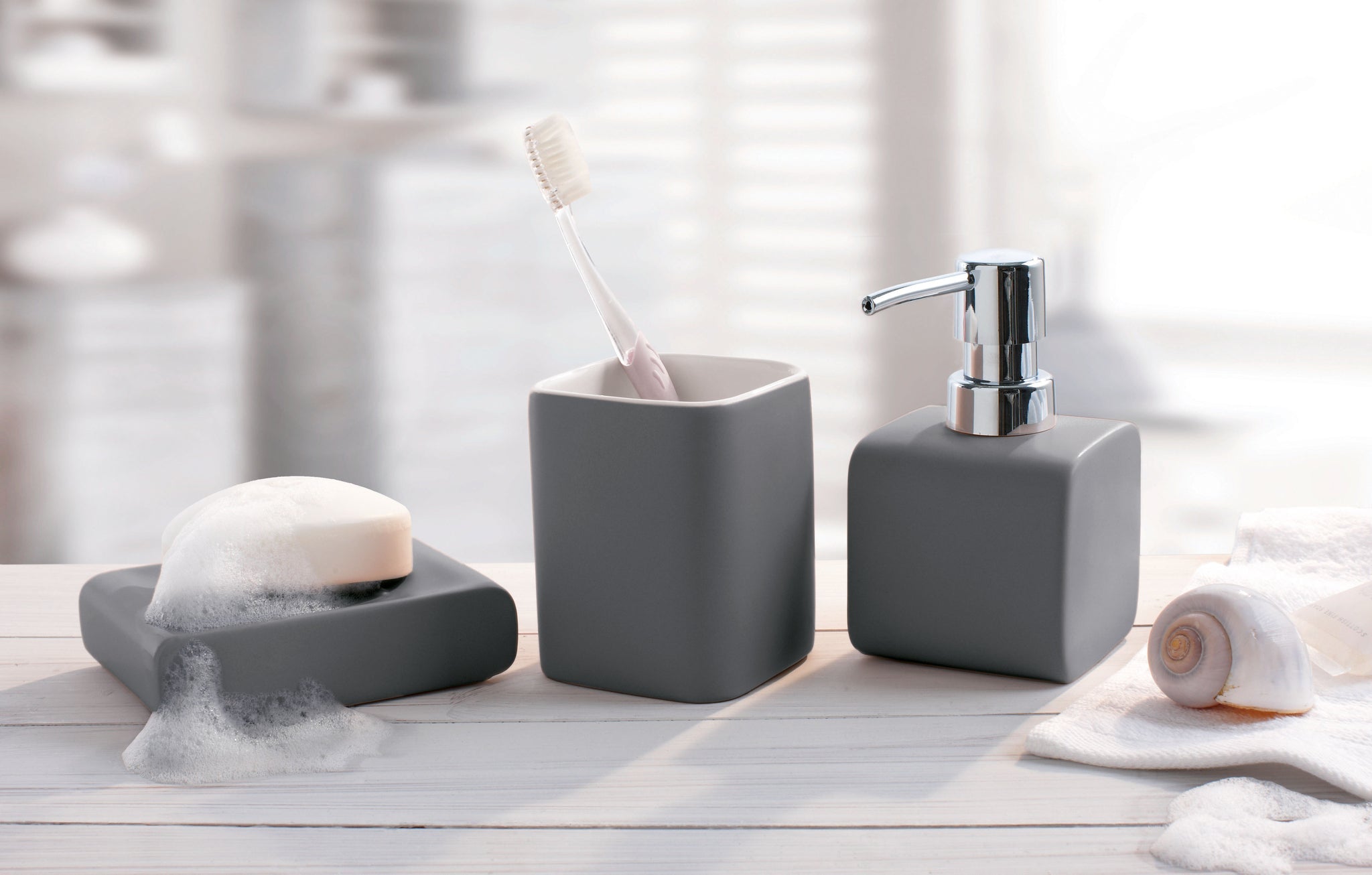 Graue CUBIC Badaccessoires mit Seifenspender, Zahnbürstenbecher und Seifenschale auf Waschtisch.