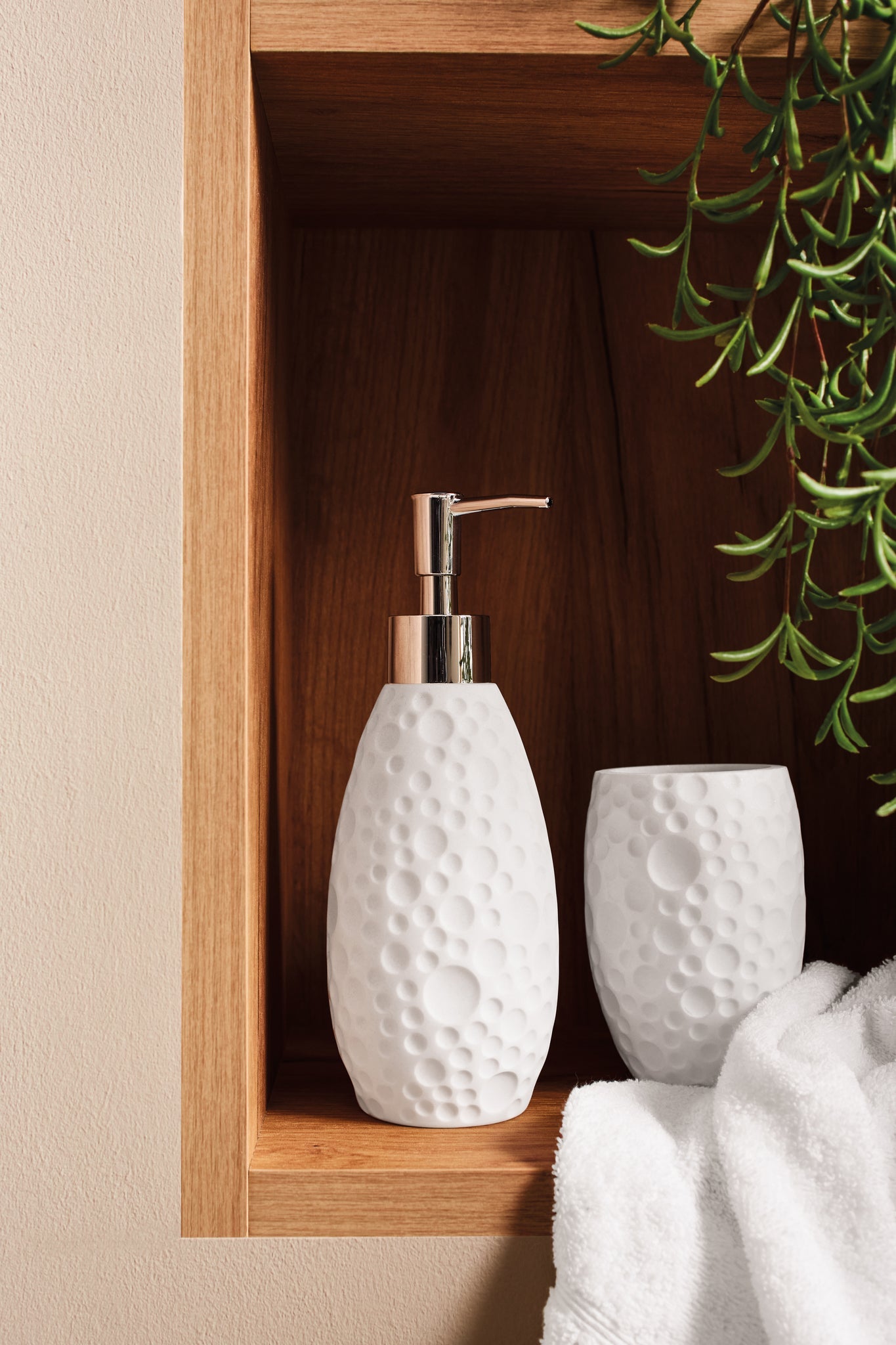 Weißer Seifenspender und Becher in Holzablage mit Handtuch und Pflanze