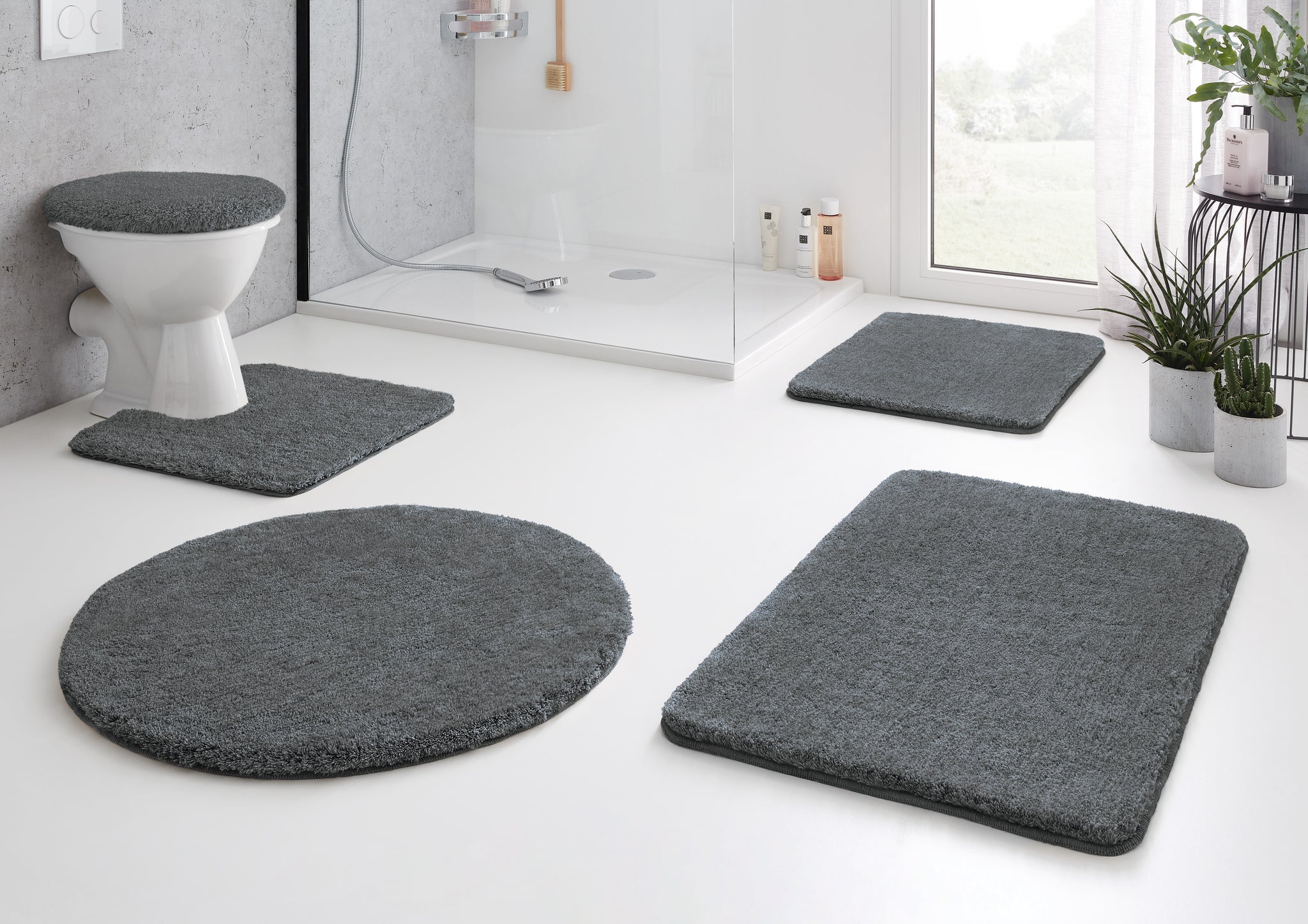 Graues fünfteiliges Badteppich-Set vor Dusche und WC im modernen Bad