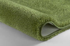 Detailansicht eines grünen, hochflorigen Badteppichs auf hellem Boden