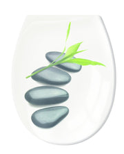 Weiße Seifenschale mit vier schwarzen Steinen und grünem Bambusblatt