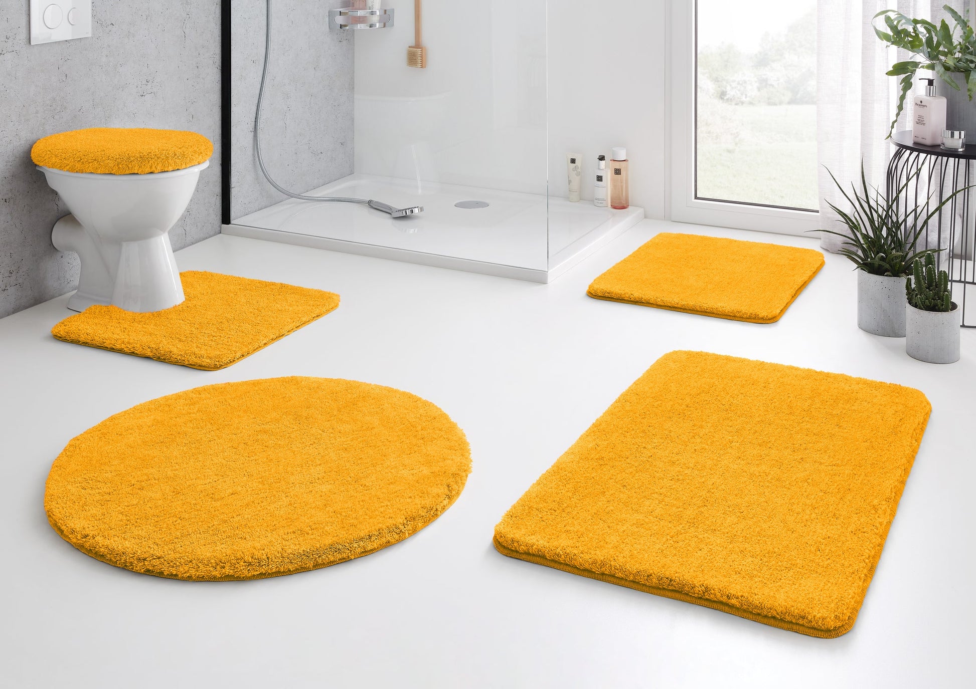 Gelbe Badematten-Garnitur im Bad mit Dusche und WC auf hellem Boden