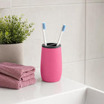 Ein pinker Zahnputzbecher mit zwei Zahnbürsten steht am Waschbecken.