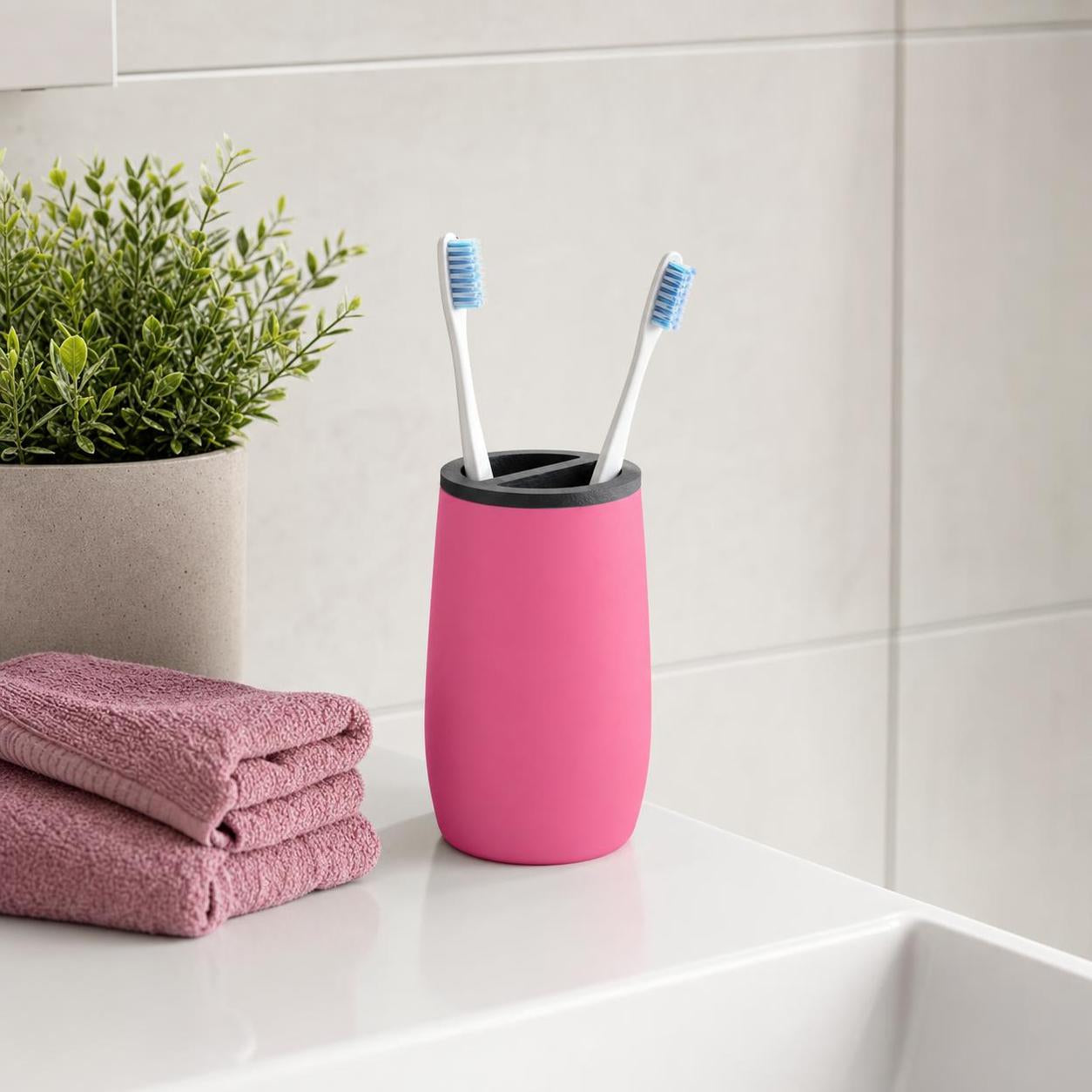 Ein pinker Zahnputzbecher mit zwei Zahnbürsten steht am Waschbecken.