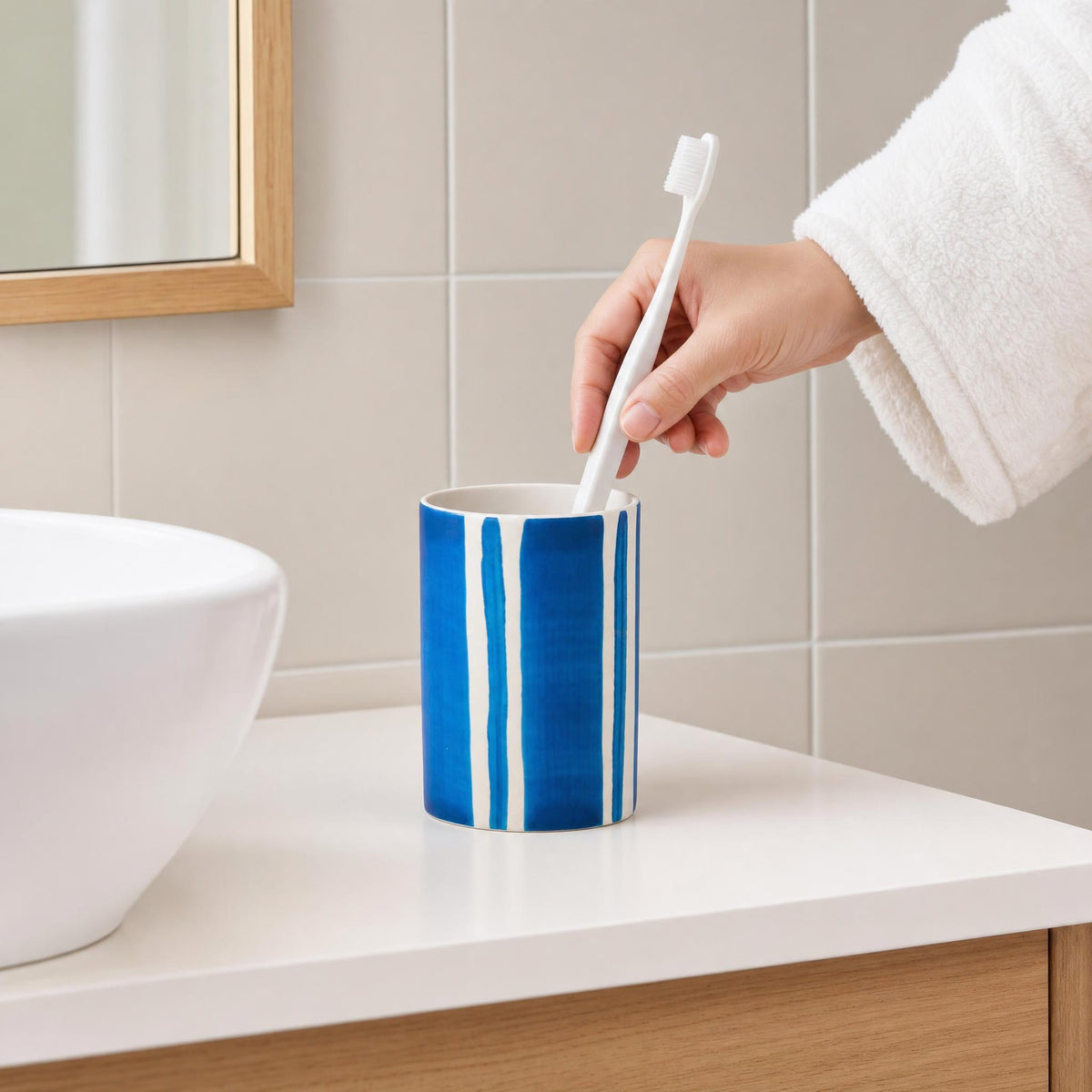 Hand mit Zahnbürste über blau-weißem Becher auf Badablage.