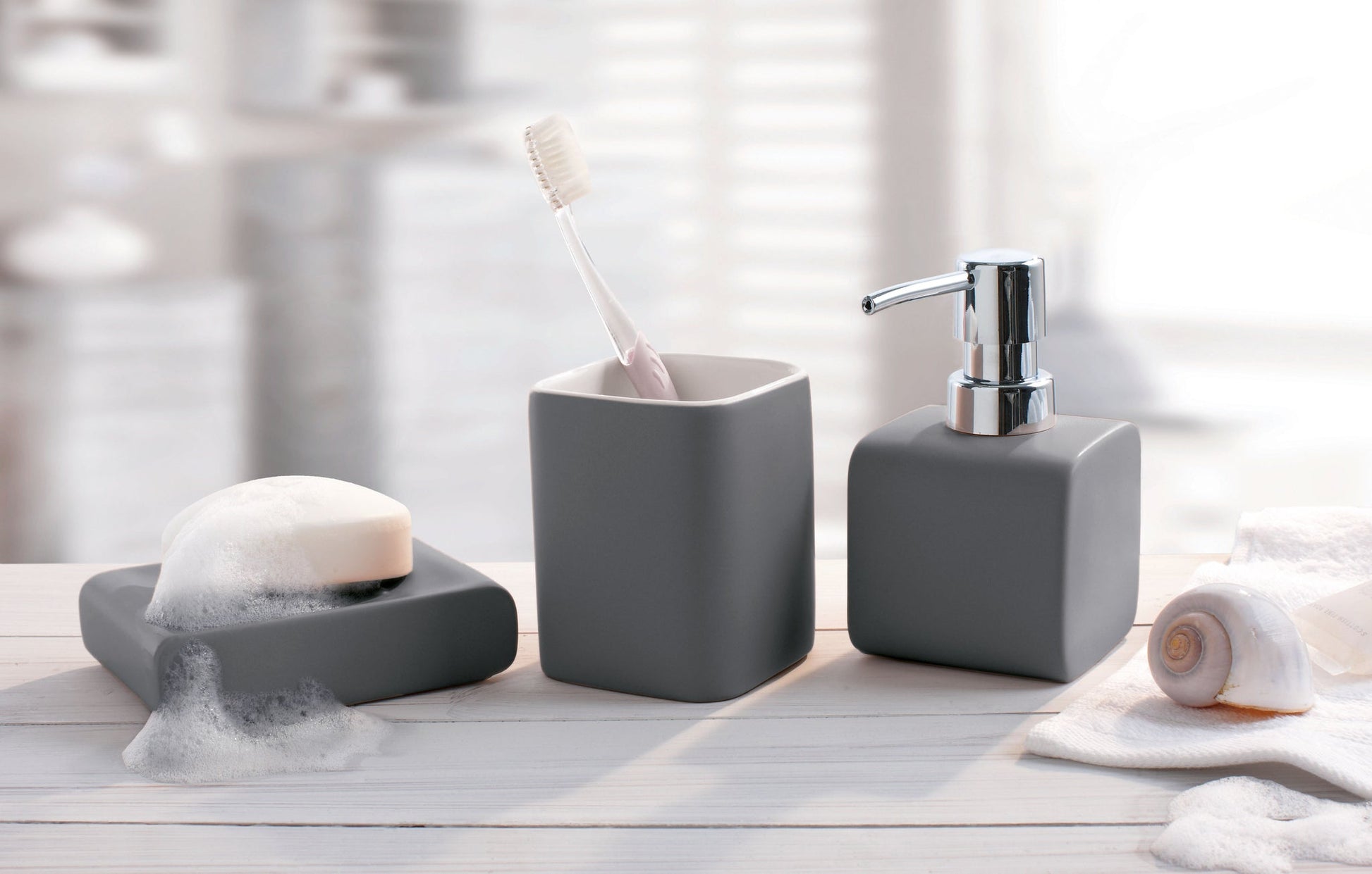 Zahnputzbecher CUBIC Anthrazit mit Zahnbürste auf Waschbecken neben Seifenspender und Seifenschale.