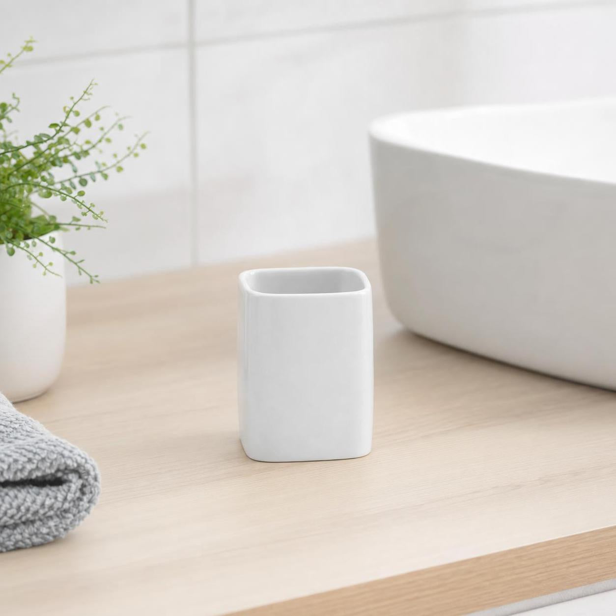 Weißer Zahnputzbecher steht auf hellem Waschtisch neben Waschbecken.