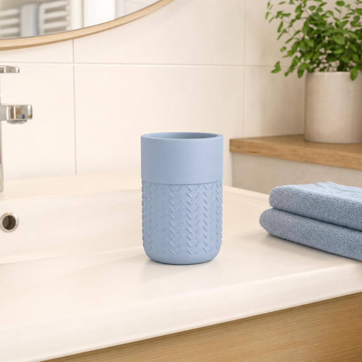 Blauer Zahnputzbecher mit Struktur steht auf dem Waschbecken.