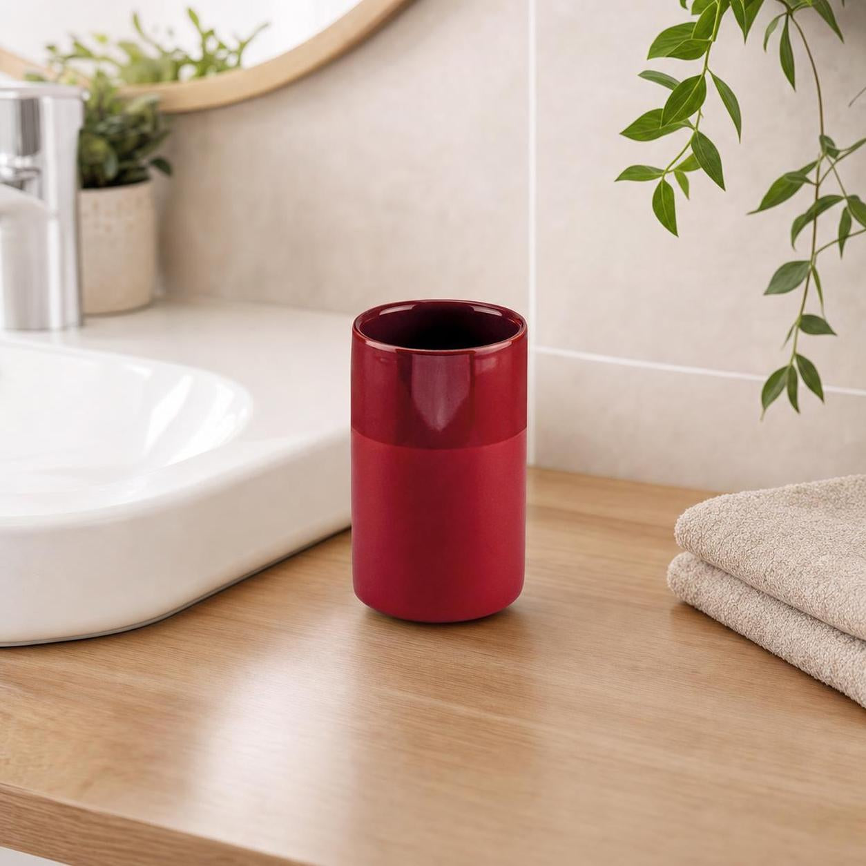 Roter Zahnputzbecher steht auf Holzablage neben Waschbecken und Handtüchern.