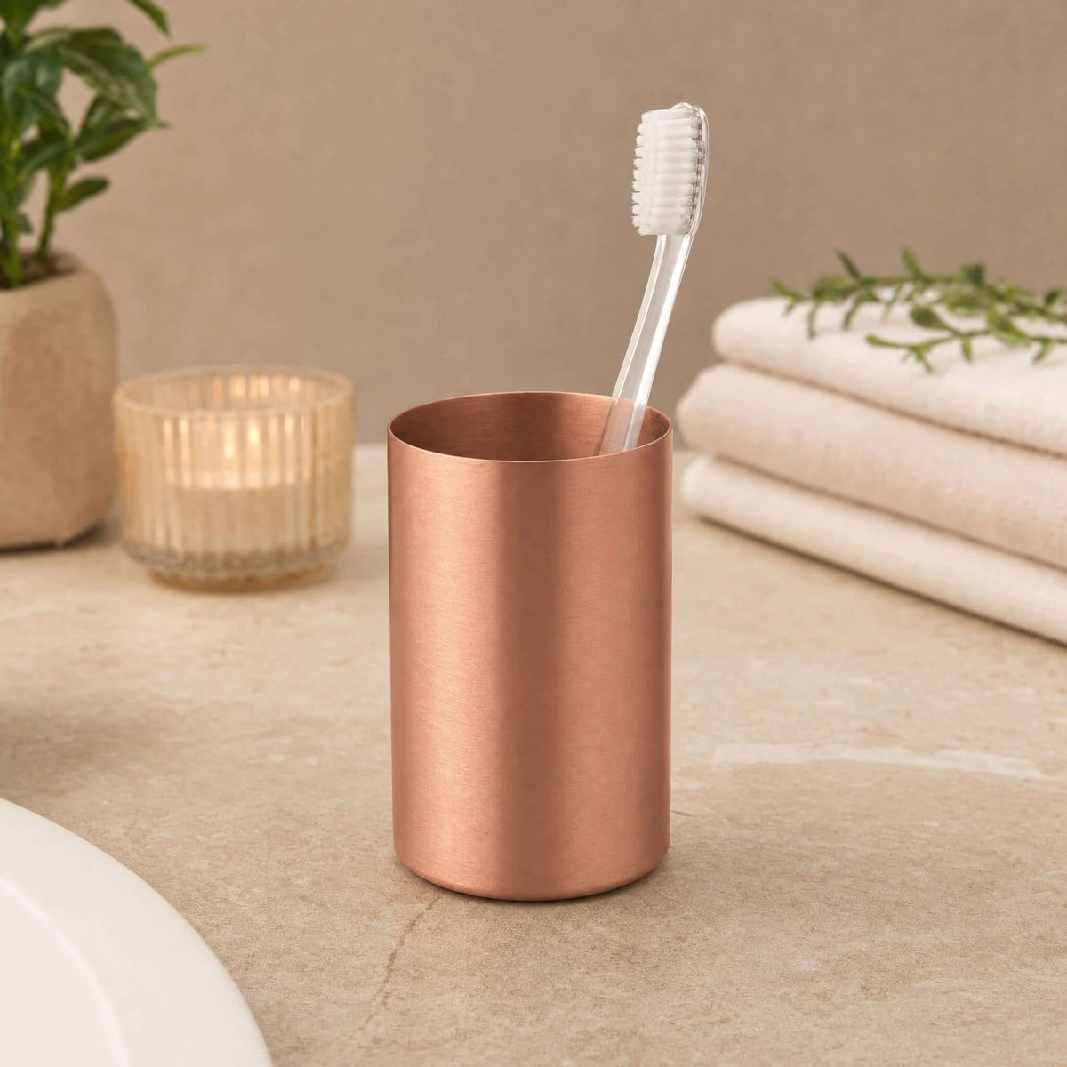 Roségoldfarbener Zahnputzbecher mit Zahnbürste auf Waschbeckenablage.