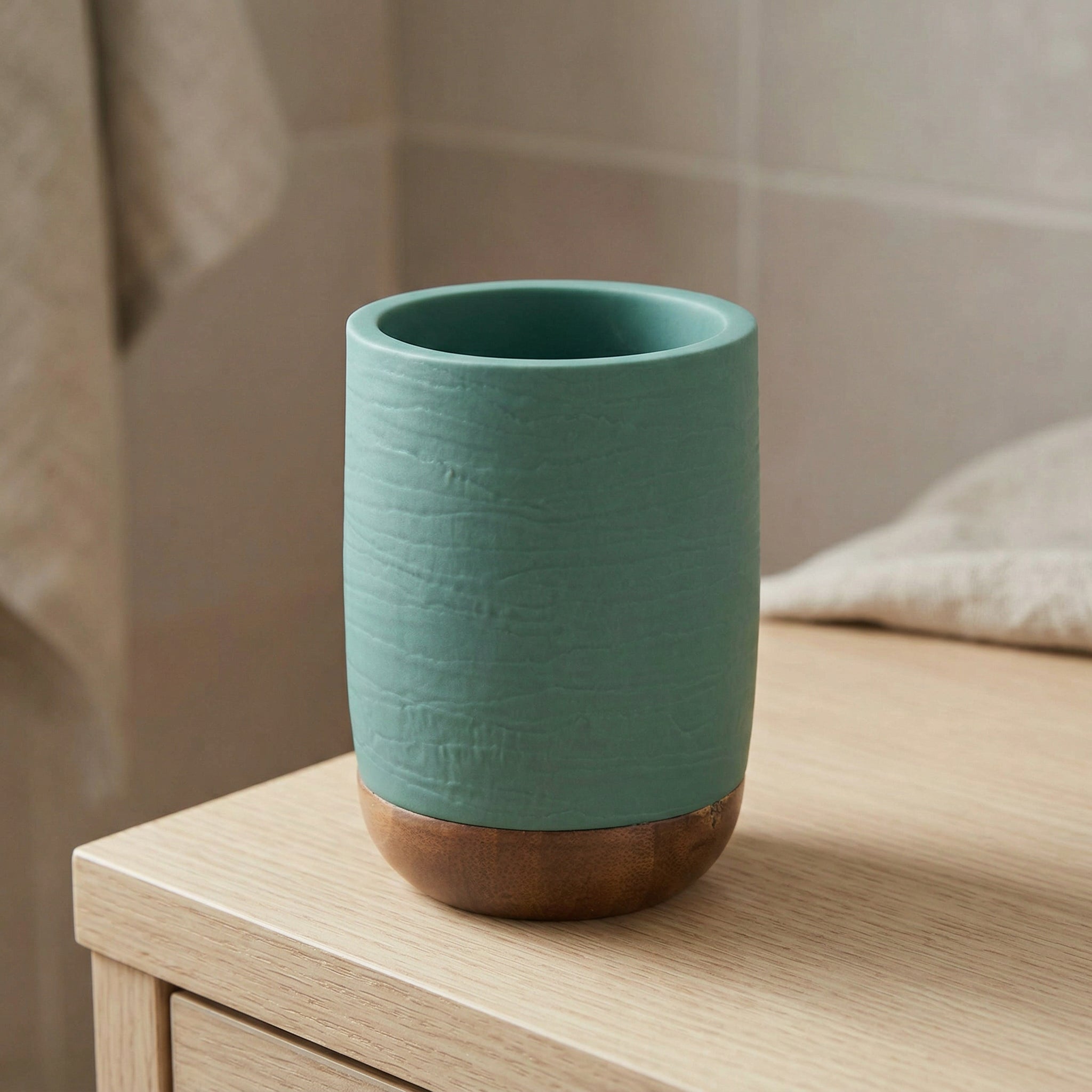 Grüner Zahnputzbecher mit Holzfuß auf hellem Badezimmerschrank stehend