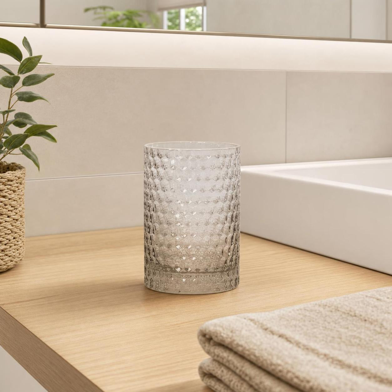 Strukturierter Glasbecher steht auf Holzablage im Badezimmer.