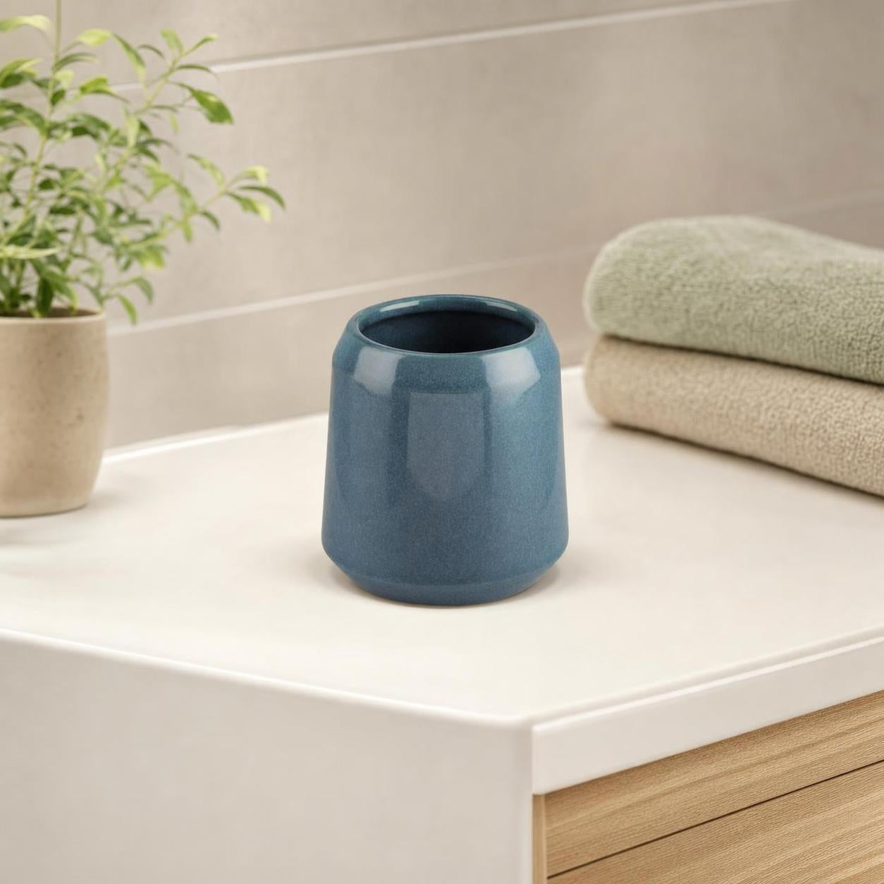 Blauer Zahnputzbecher steht auf dem Waschbecken neben Handtüchern.
