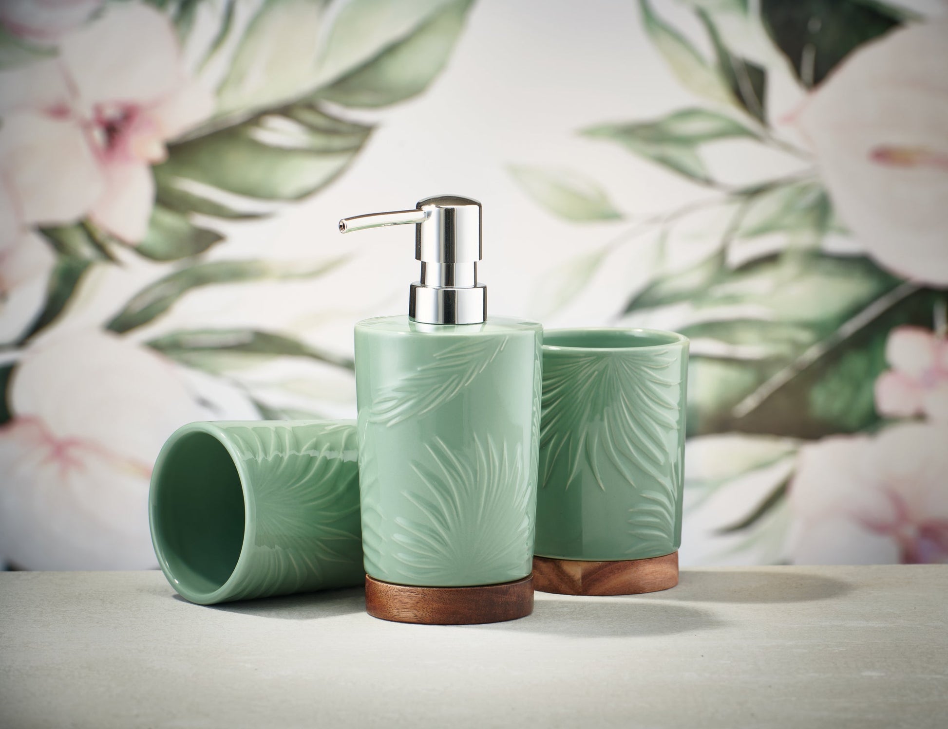 Zahnputzbecher PALM Maledivia mit passendem Seifenspender vor floralem Hintergrund aufgestellt.