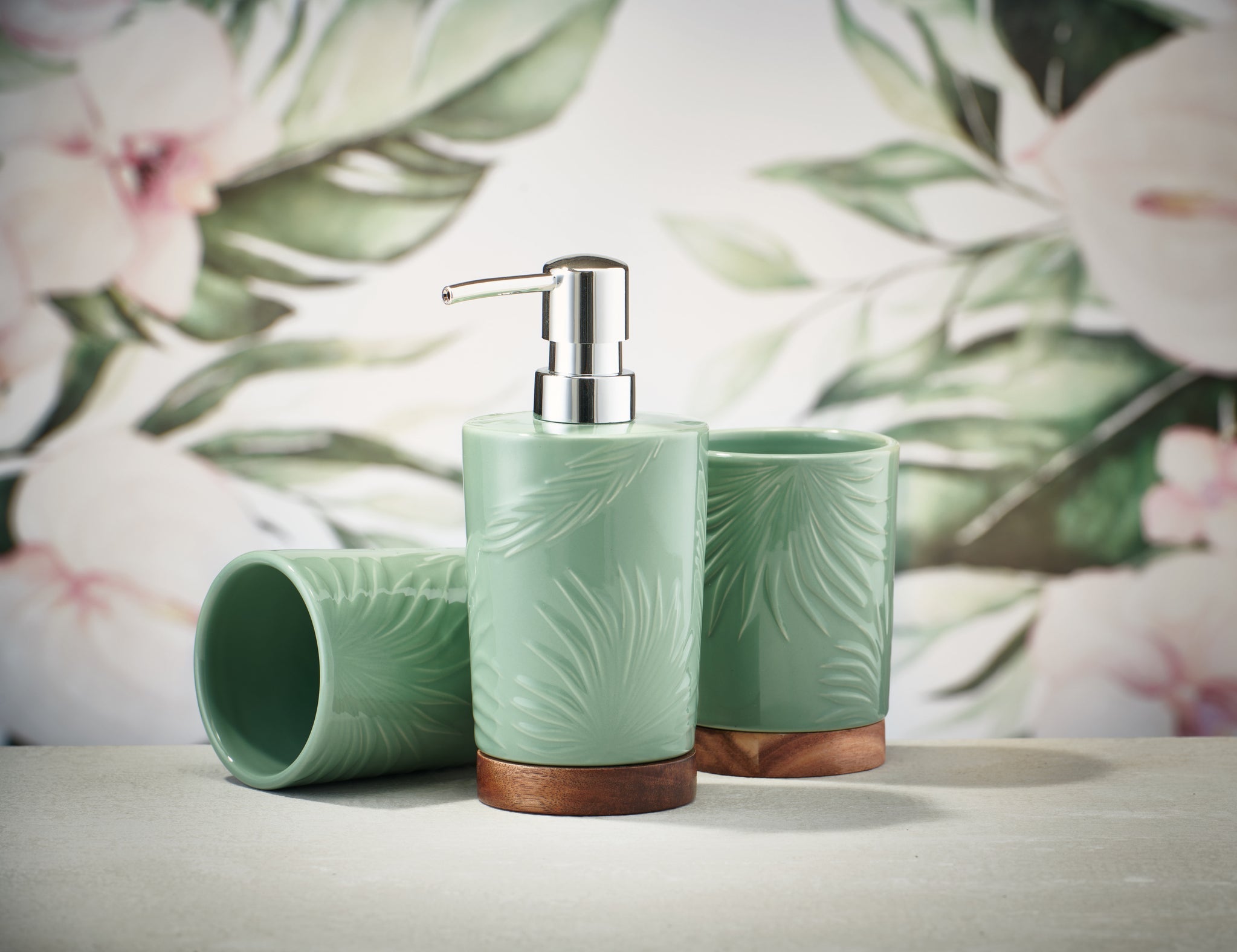 Zahnputzbecher PALM Maledivia mit passendem Seifenspender vor floralem Hintergrund aufgestellt.