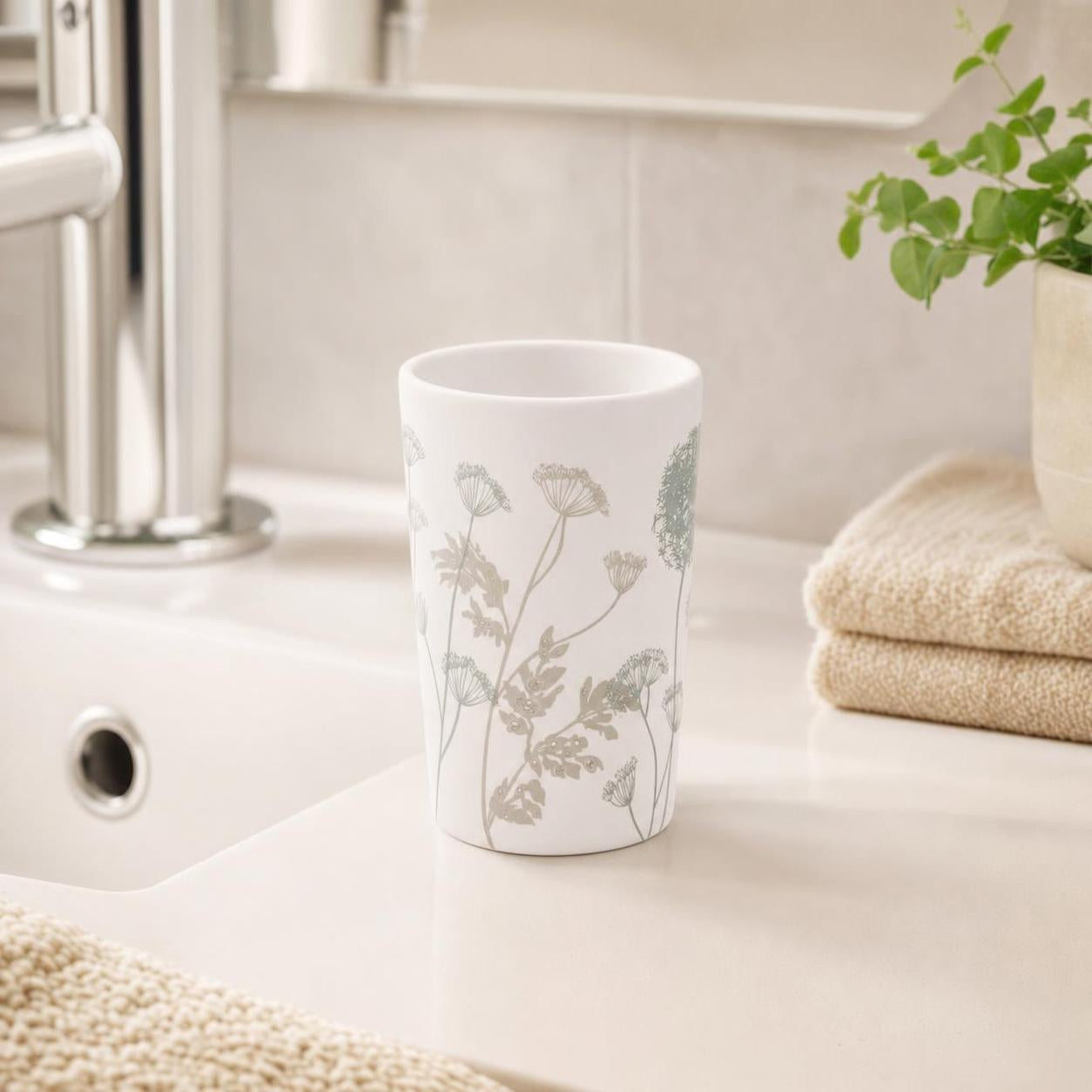 Weißer Zahnputzbecher mit Blumenmuster steht am Waschbecken.