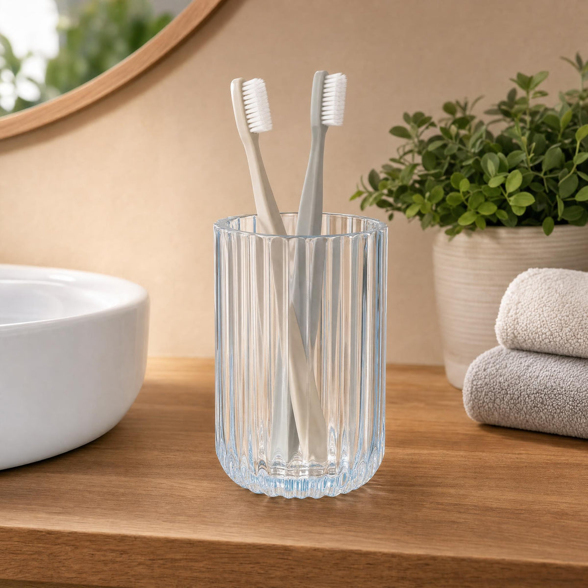 Zwei Zahnbürsten im geriffelten Glasbecher auf einem Badezimmerregal.