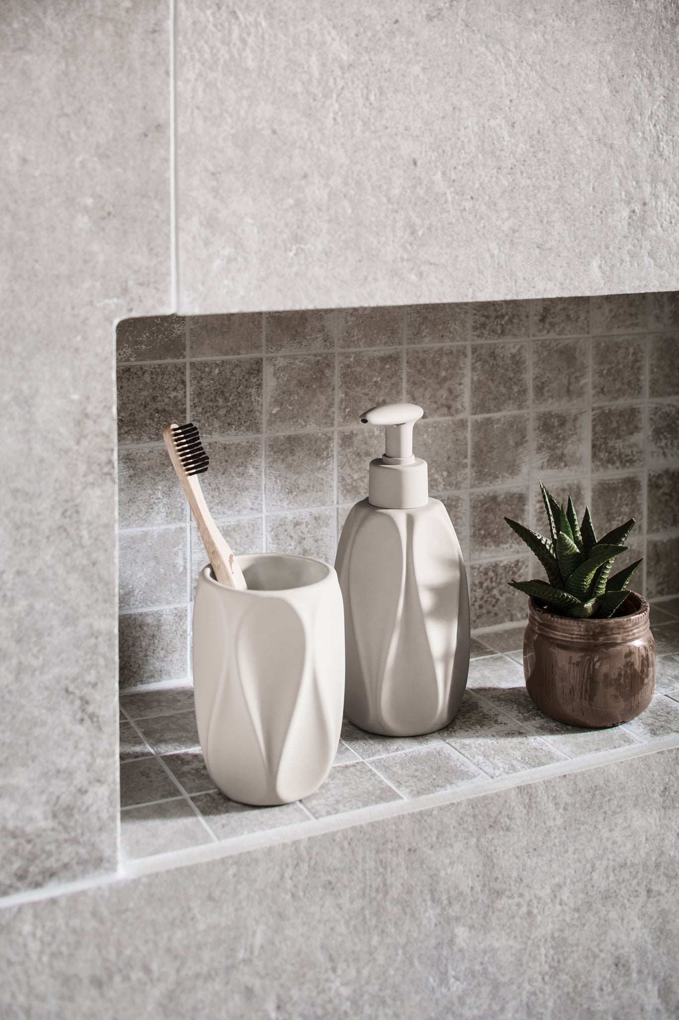 Zahnputzbecher TREVI Seidenfarben mit Holz-Zahnbürste in grauer Badezimmernische neben Seifenspender.