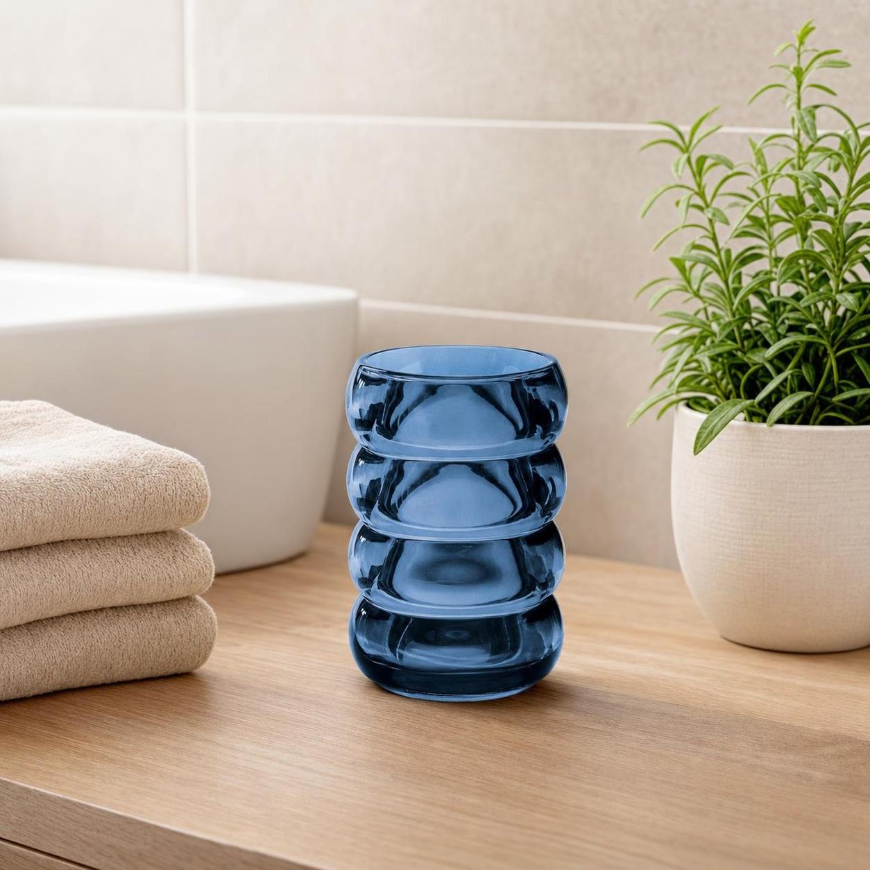 Ein blauer Glasbecher steht im Bad neben Handtüchern und Pflanze.