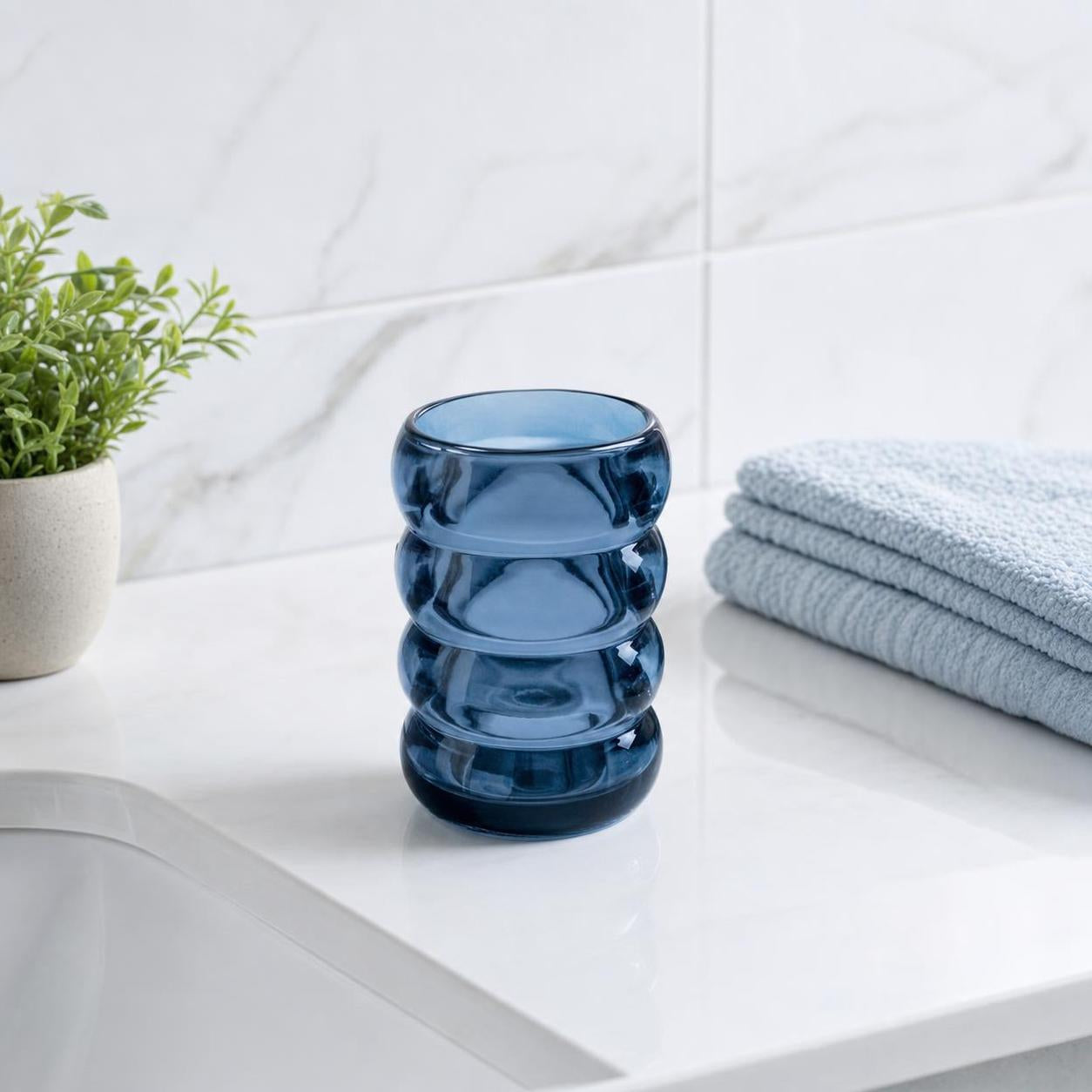 Blauer Glasbecher steht neben Handtüchern auf dem Badwaschtisch.