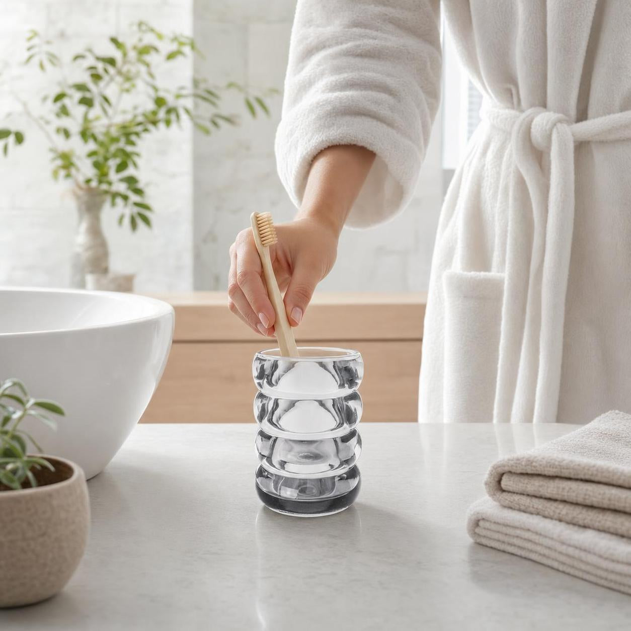 Ein gerillter Glas-Zahnputzbecher hält eine Holzzahnbürste im Bad.