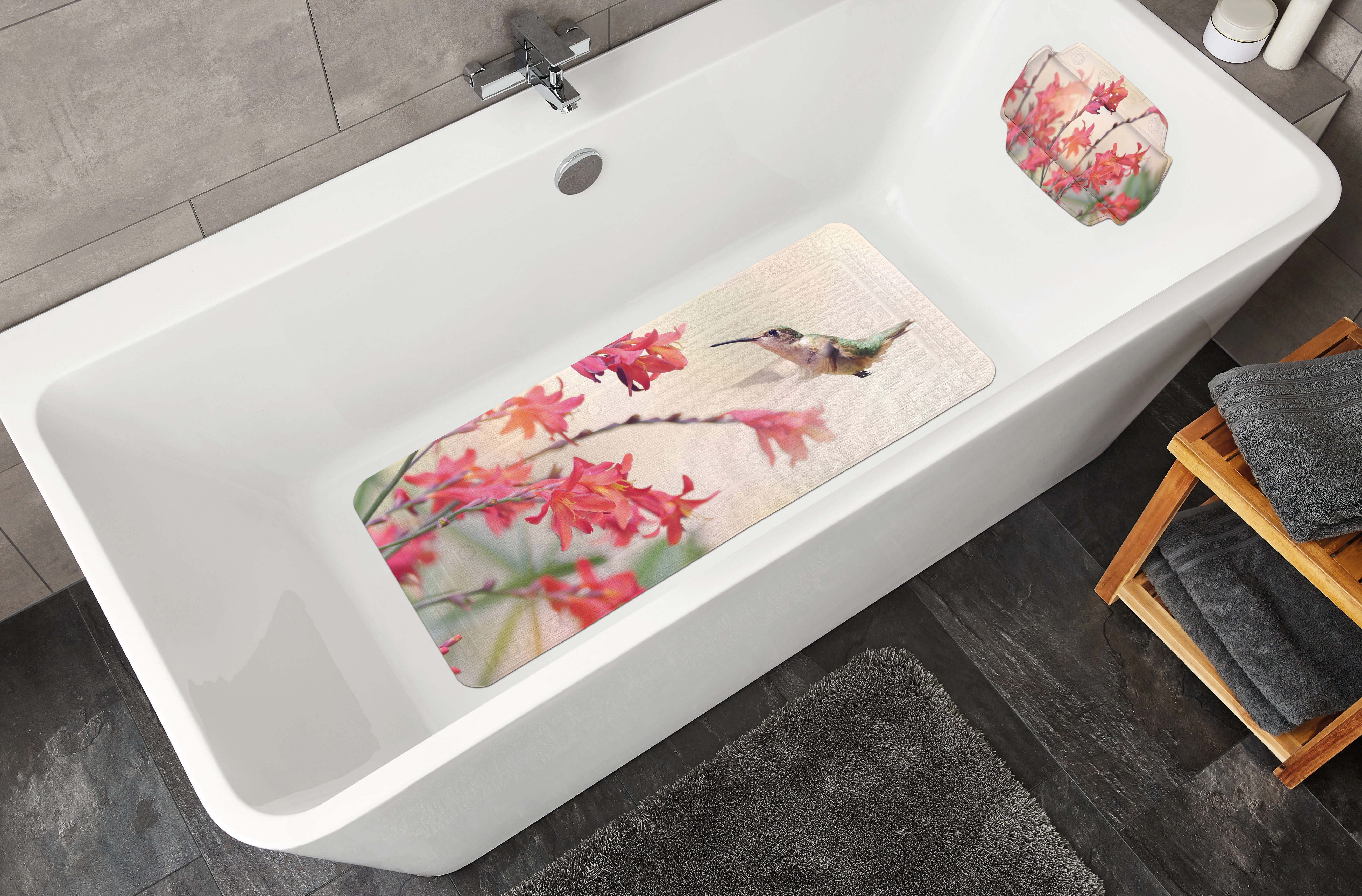 Badezimmer mit weißer Badewanne, dekoriert mit einer Badematte und einem Kissen, beide mit Kolibri- und Blumenmotiv.