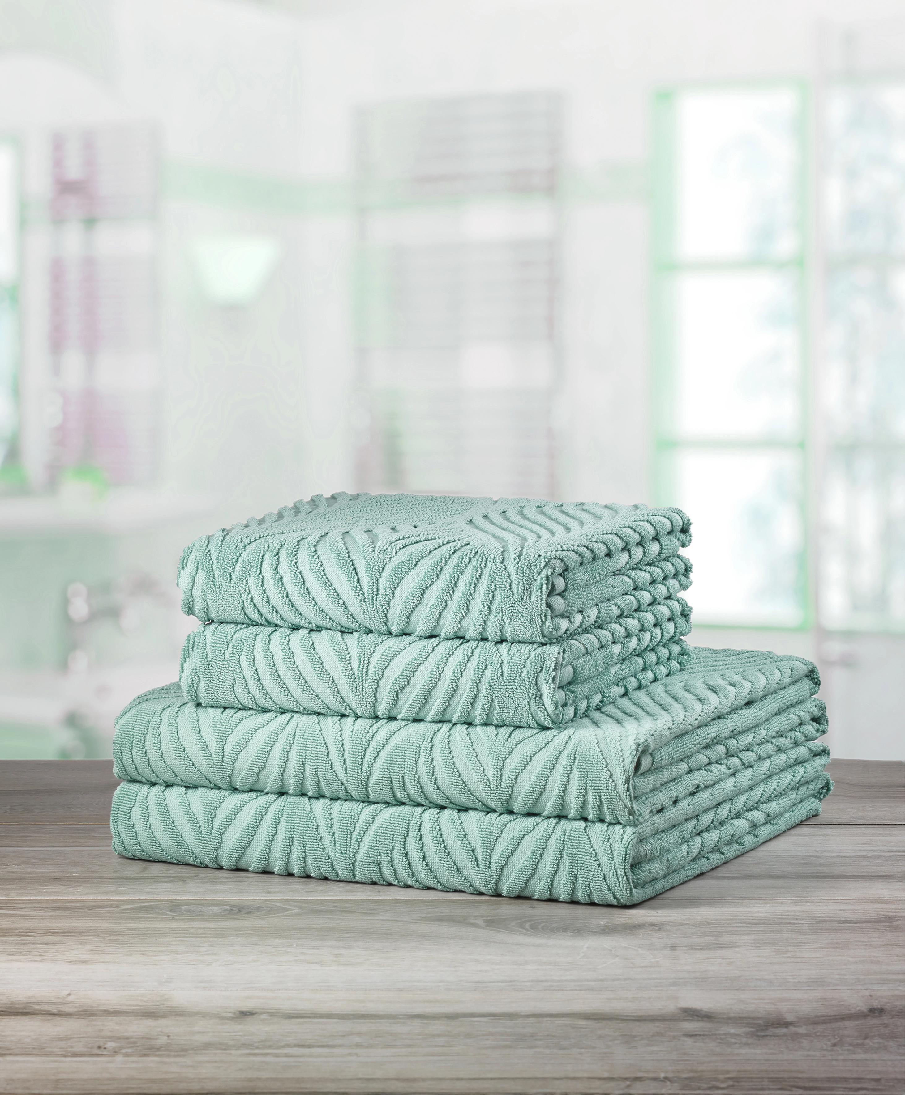 Handtuch-Set in Mintgrün mit elegantem Blattmuster, dekorativ auf einem Holztisch gestapelt.