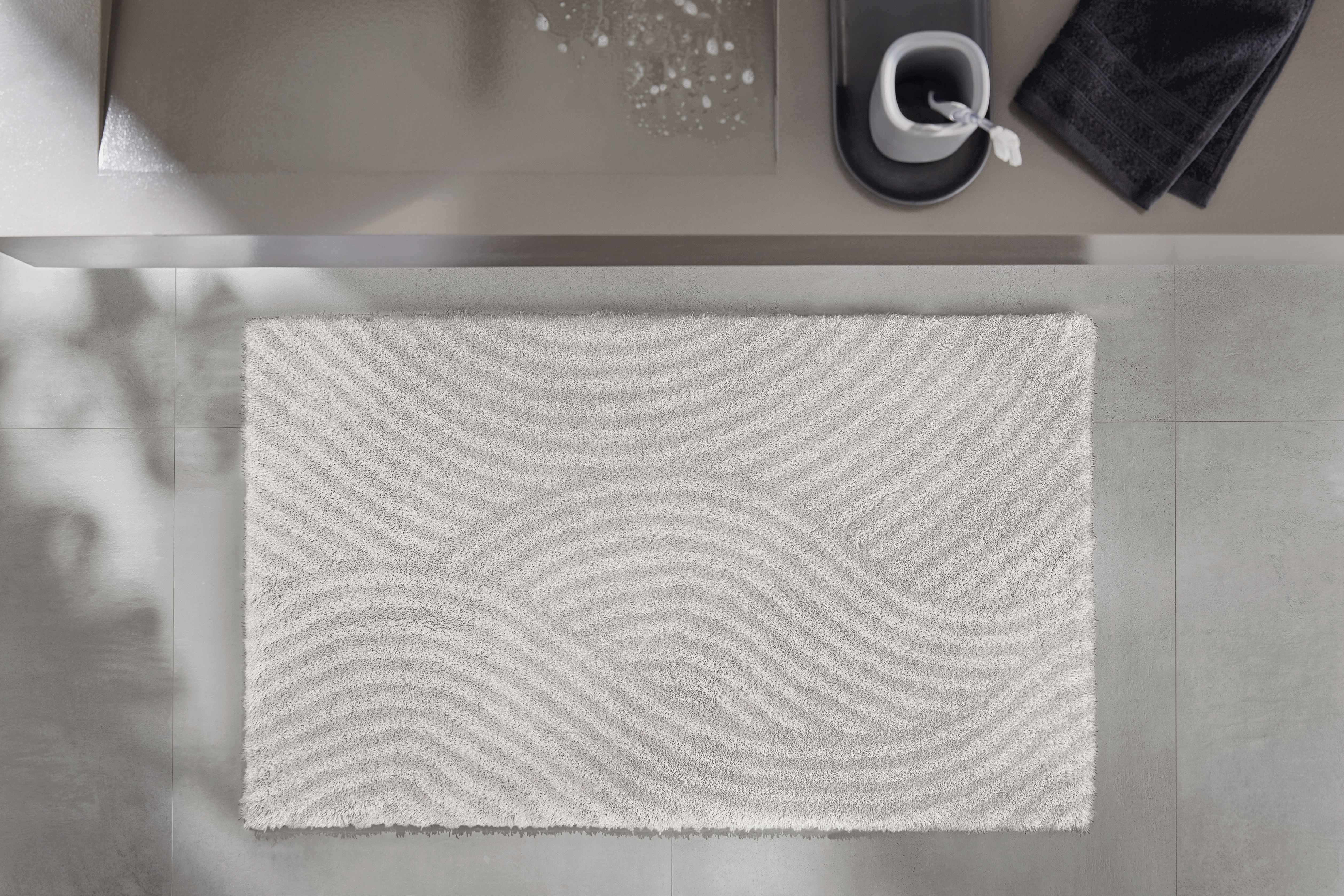 Weißer Badteppich mit wellenförmigem Muster, platziert vor einem modernen Waschbecken. Ideal für ein stilvolles Badezimmer.