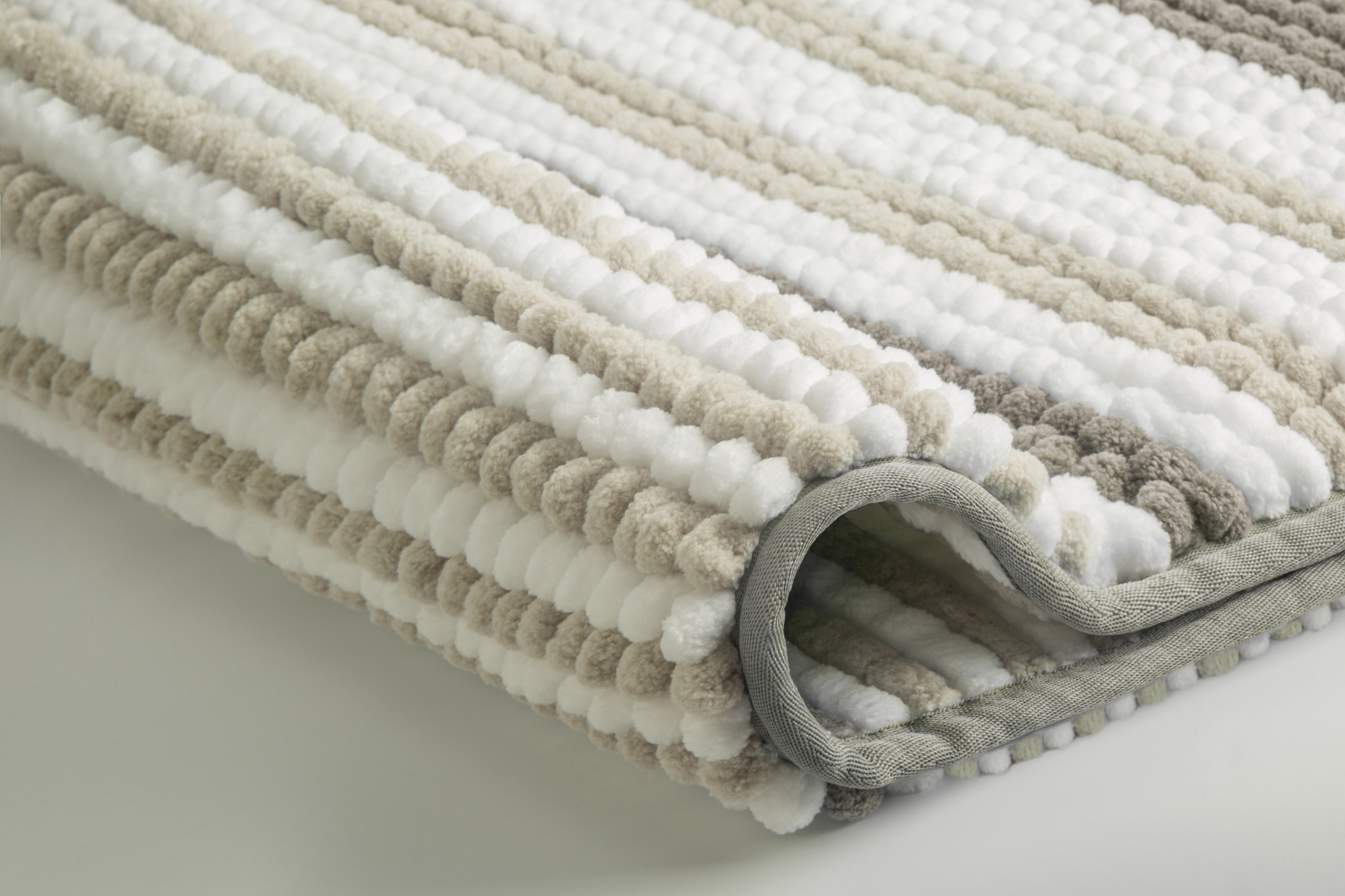 Weicher, gestreifter Badteppich in Beige, Weiß und Grau mit strukturierter Oberfläche und rutschfester Unterseite.