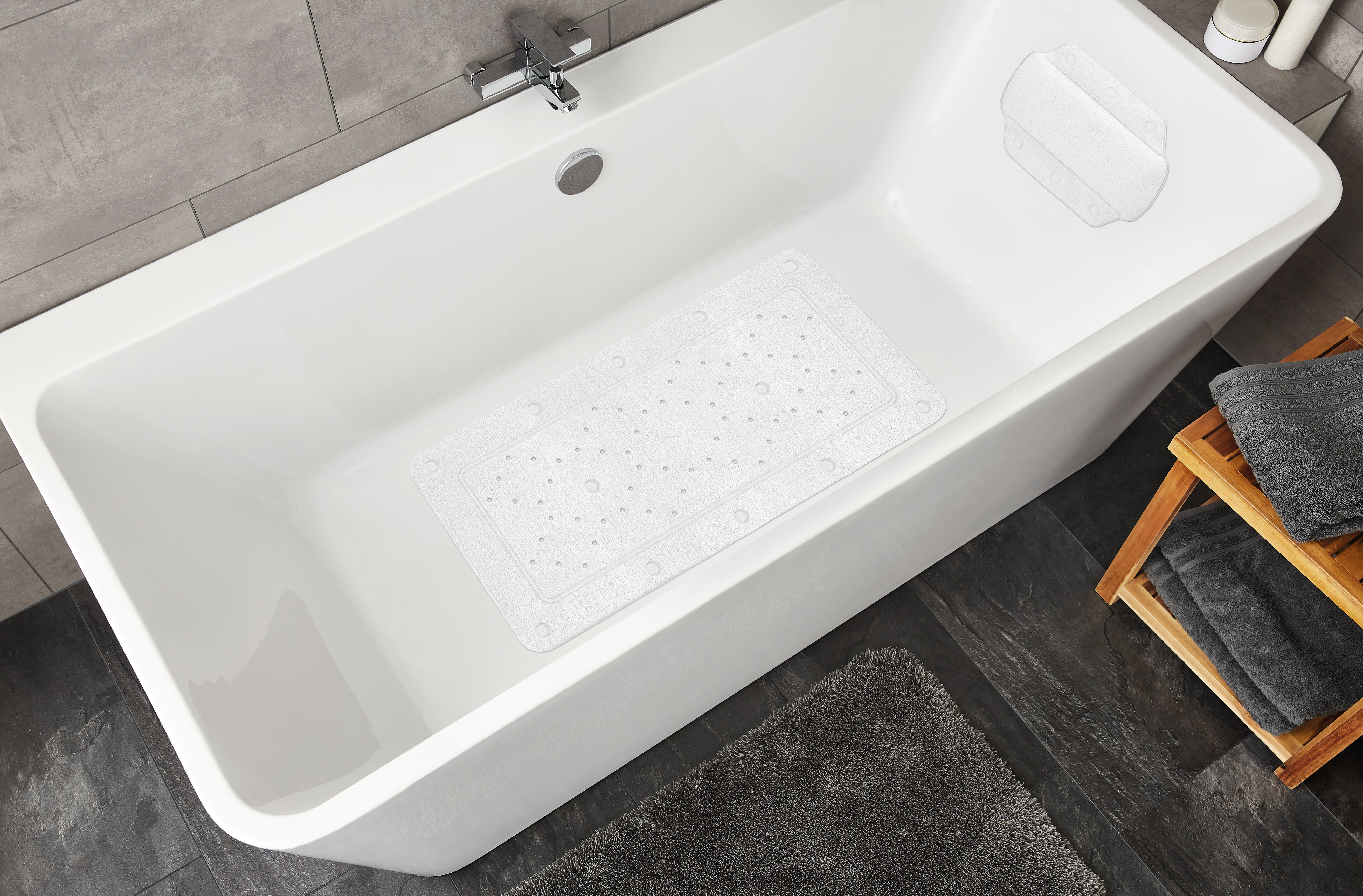 Weiße Badewanne mit rutschfester Badematte, grauem Handtuch und Holzregal in modernem Badezimmer.
