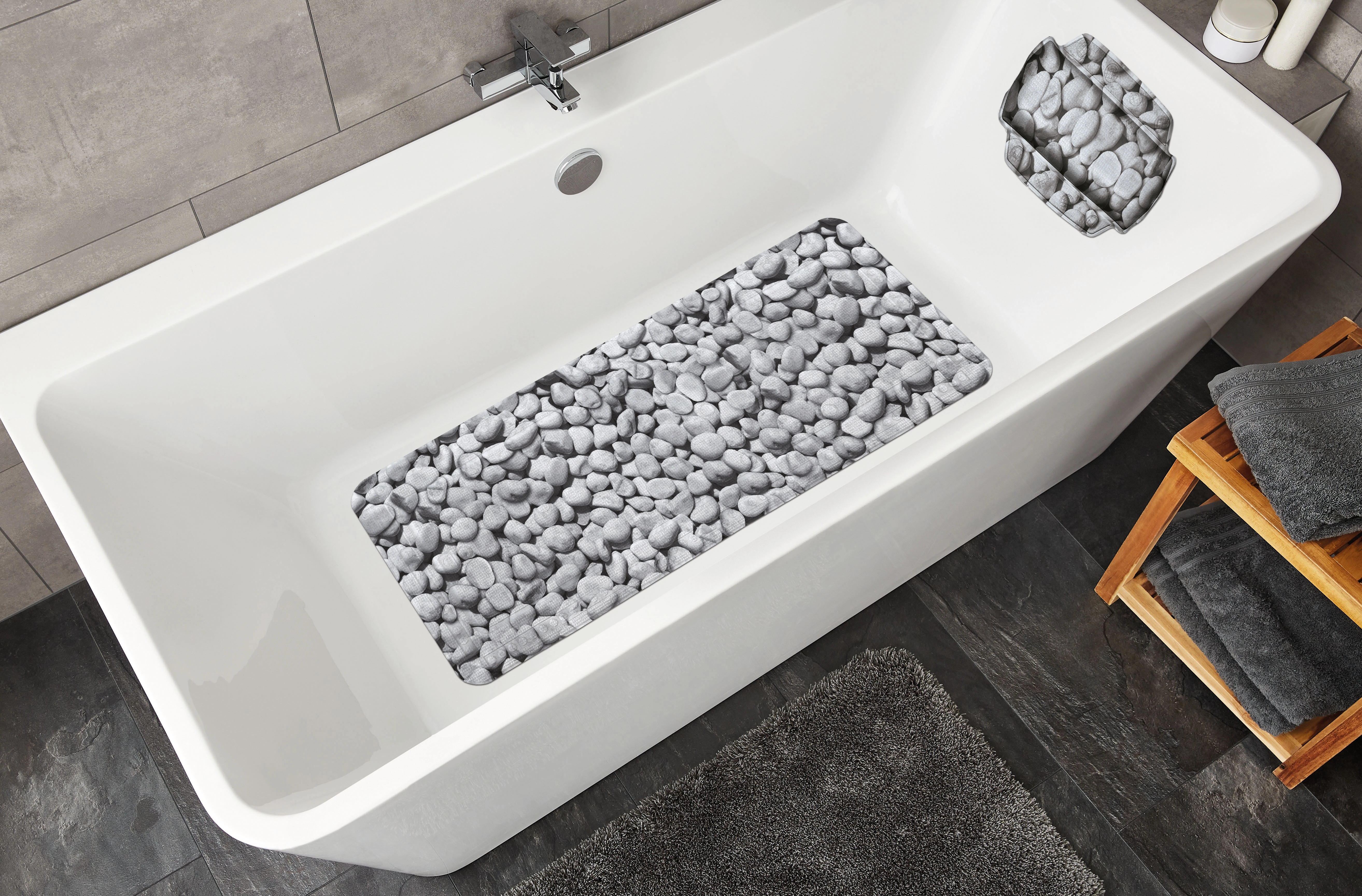 Badewannenmatte mit Kieselstein-Design in einer modernen weißen Badewanne, umgeben von grauen Fliesen und Handtüchern.
