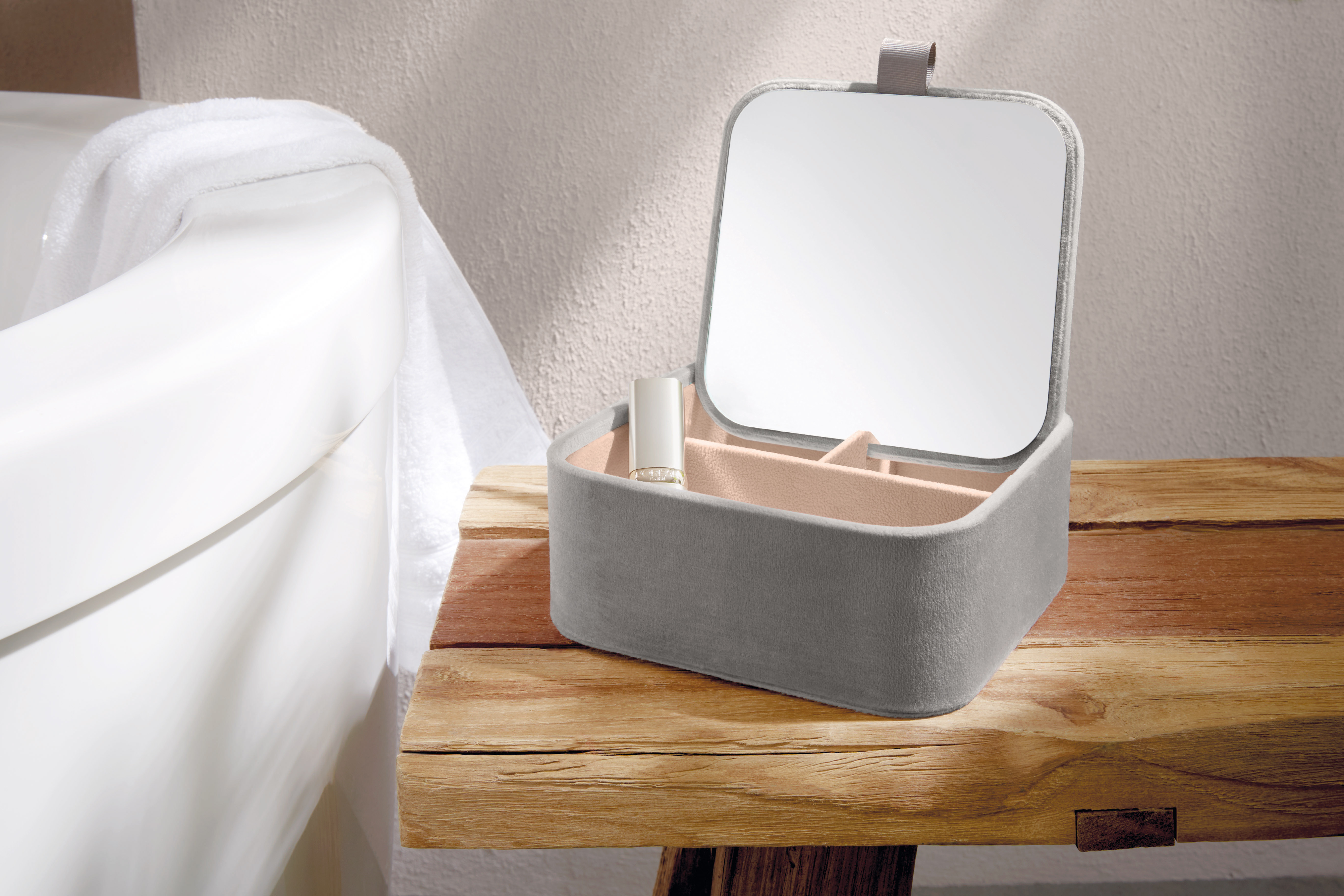 Graue Schmuckbox mit Spiegel und Fächern auf einem rustikalen Holztisch neben einer Badewanne.