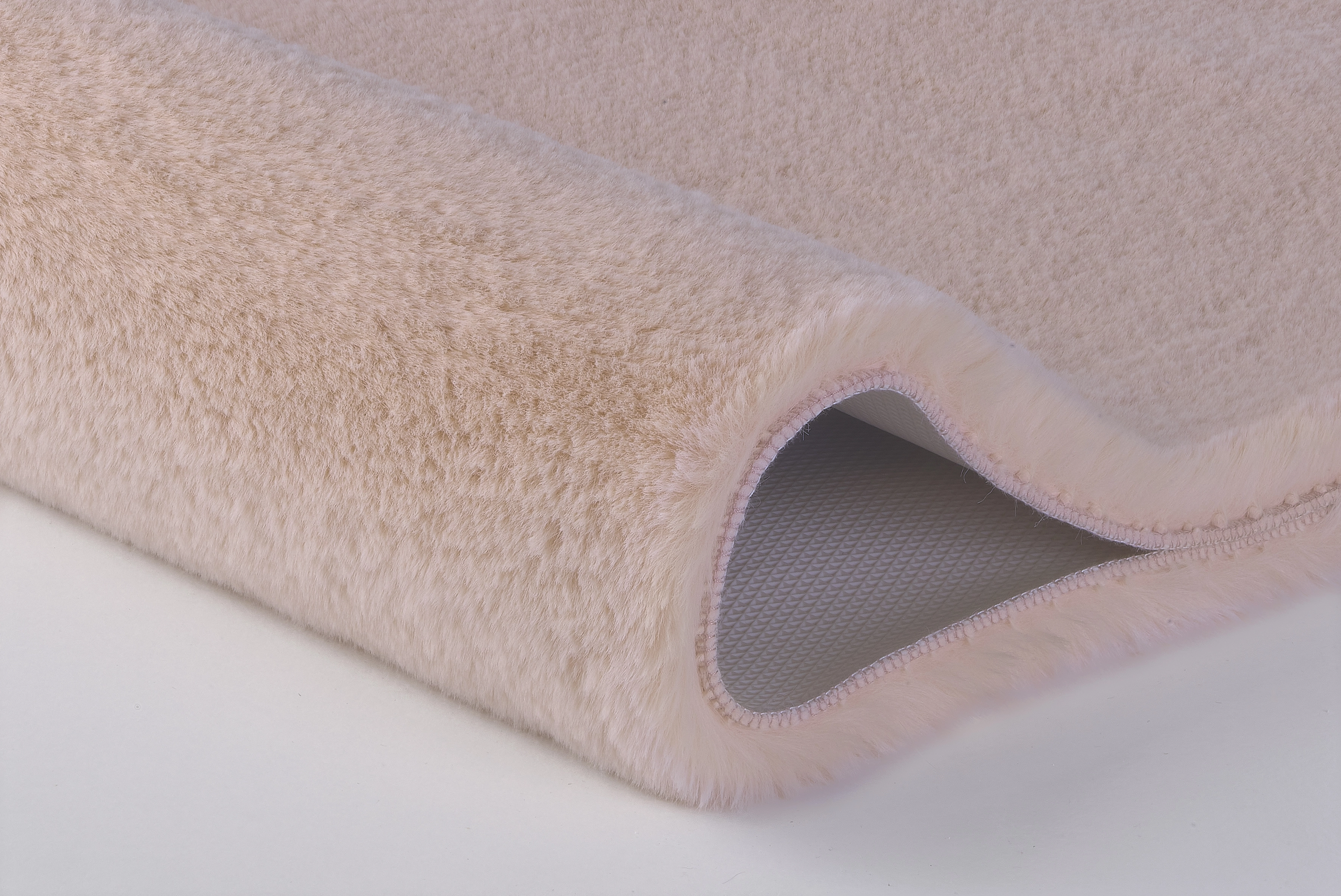 Weicher, beiger Teppich mit flauschiger Oberfläche und rutschfester Unterseite, ideal für gemütliche Wohnräume.