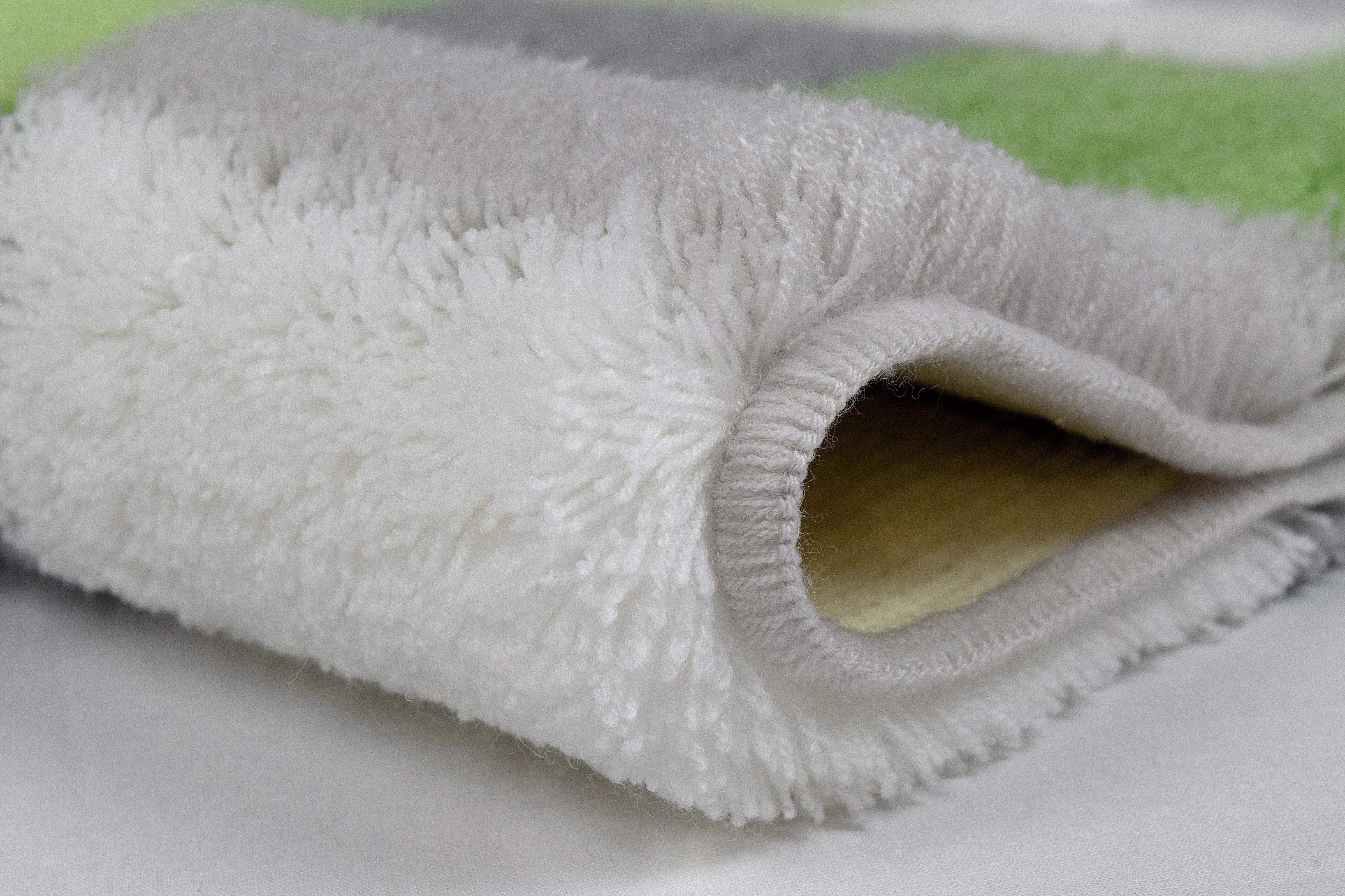 Weicher, flauschiger Teppich in Weiß, Grau und Grün, ideal für Badezimmer oder Wohnräume.