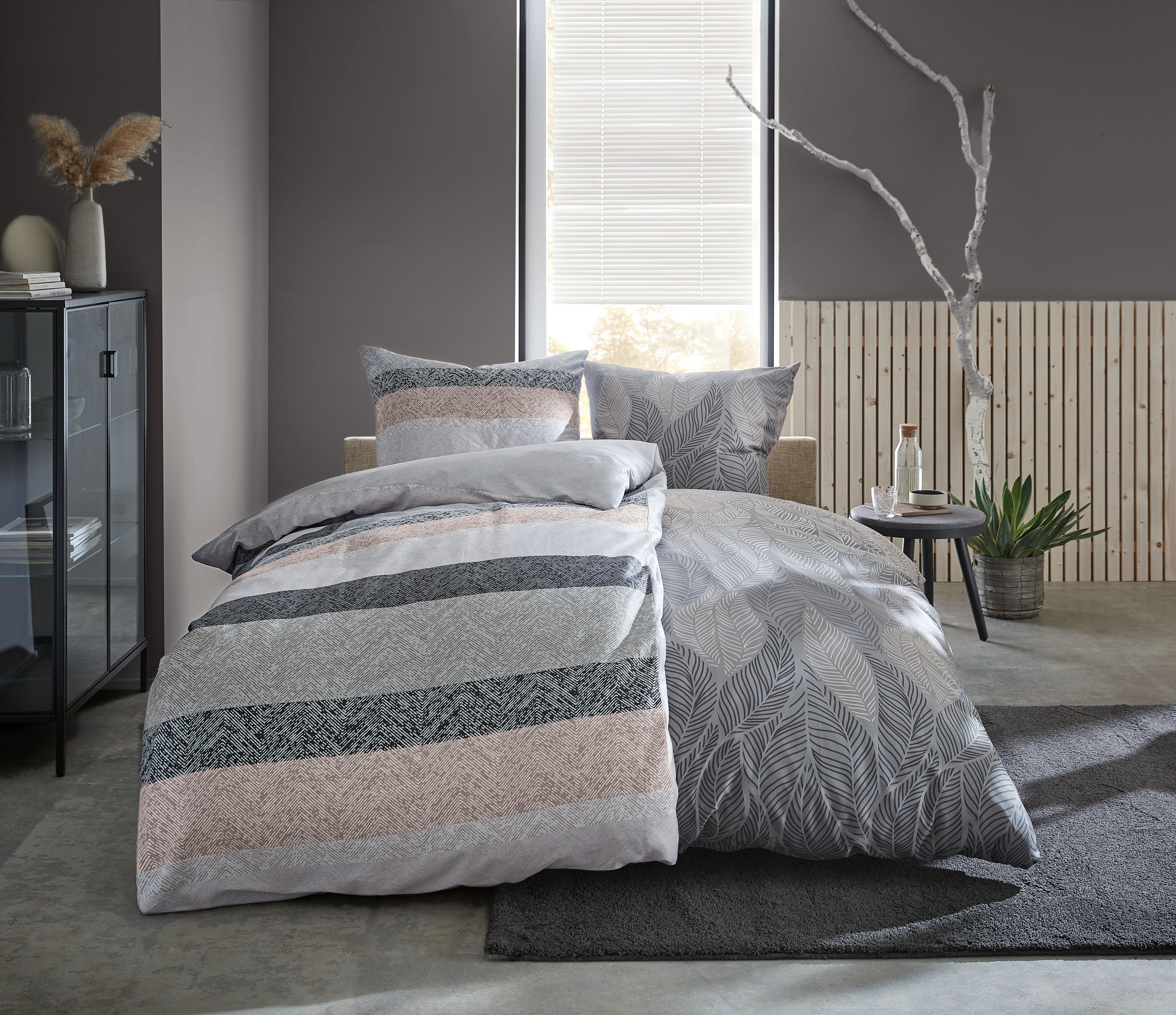 Bettwäsche-Set in Grau- und Beigetönen mit modernem Streifen- und Blättermuster, dekoriert in einem stilvollen Schlafzimmer.