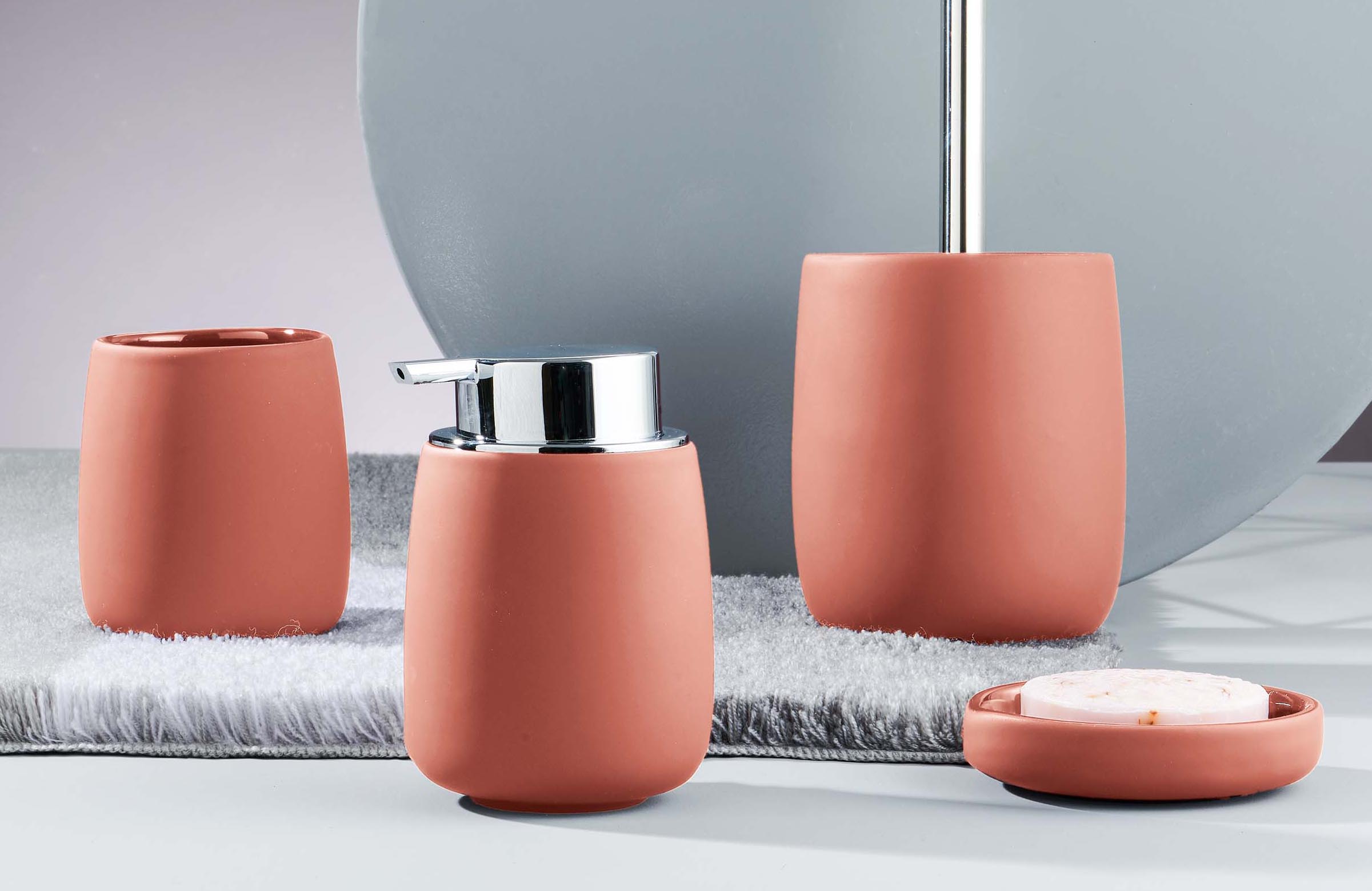 Set aus Seifenspender, Zahnbürstenhalter, Becher und Seifenschale in Terrakotta-Optik auf grauem Hintergrund.