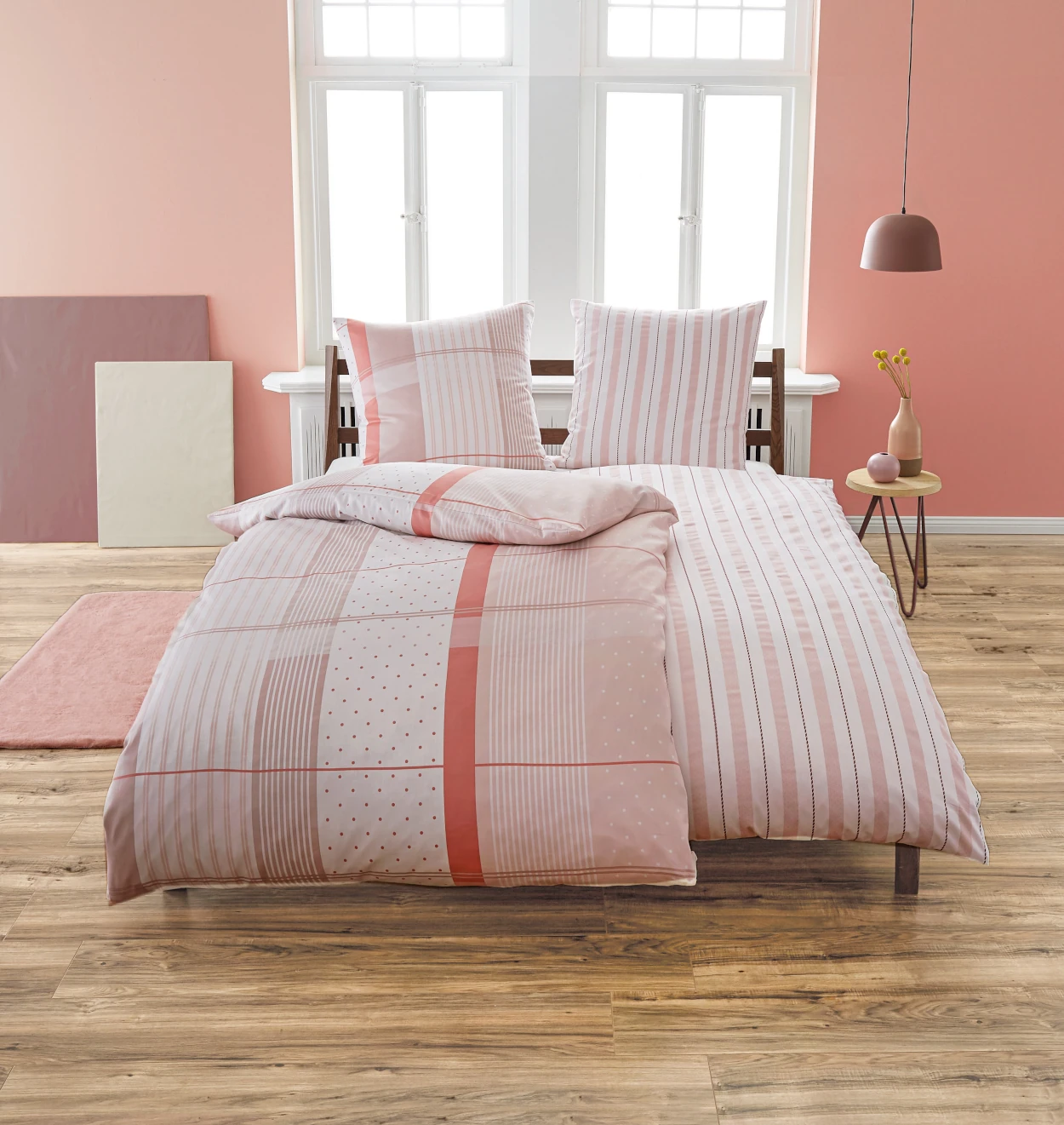 Bettwäsche-Set in Rosa mit Streifen- und Punktmuster, dekoriert in einem modernen Schlafzimmer mit Holzboden und rosa Wänden.