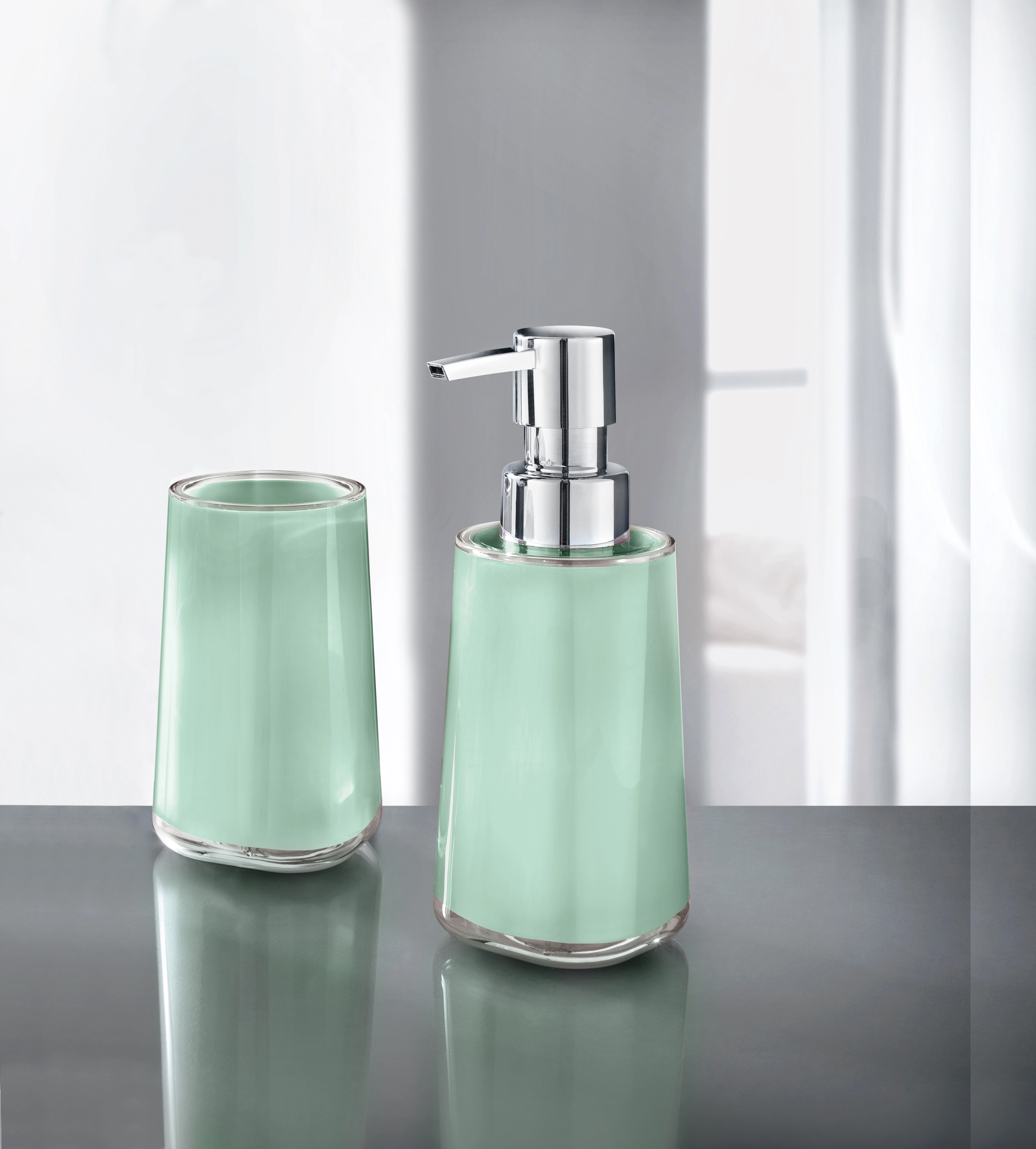 Mintgrünes Bad-Set aus Seifenspender und Zahnputzbecher aus Glas auf grauer Oberfläche vor hellem Hintergrund.