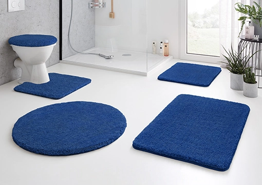 Blaue Badematte-Set in modernem Badezimmer, bestehend aus runden und rechteckigen Matten, passend für WC und Dusche.