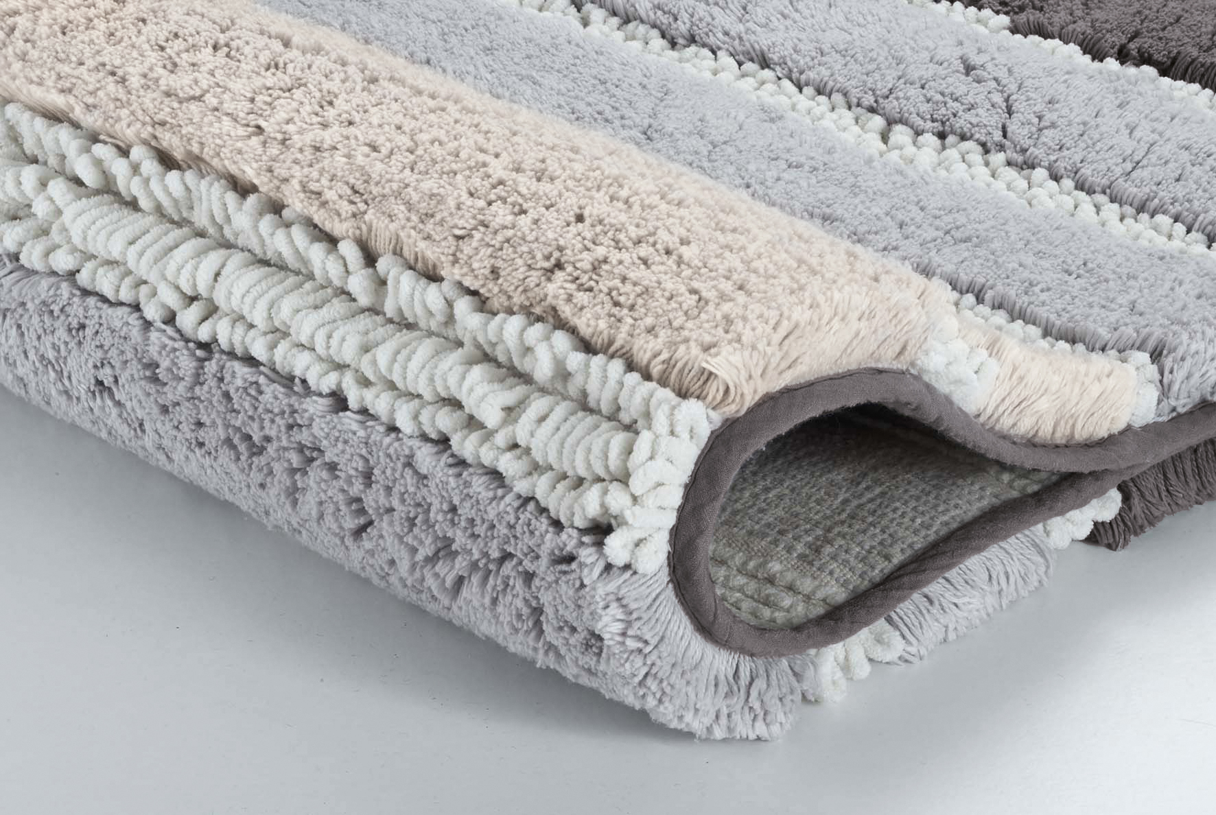 Weicher, gestreifter Badteppich in Grau- und Beigetönen, flauschige Textur, rutschfeste Unterseite, ideal für Badezimmer.