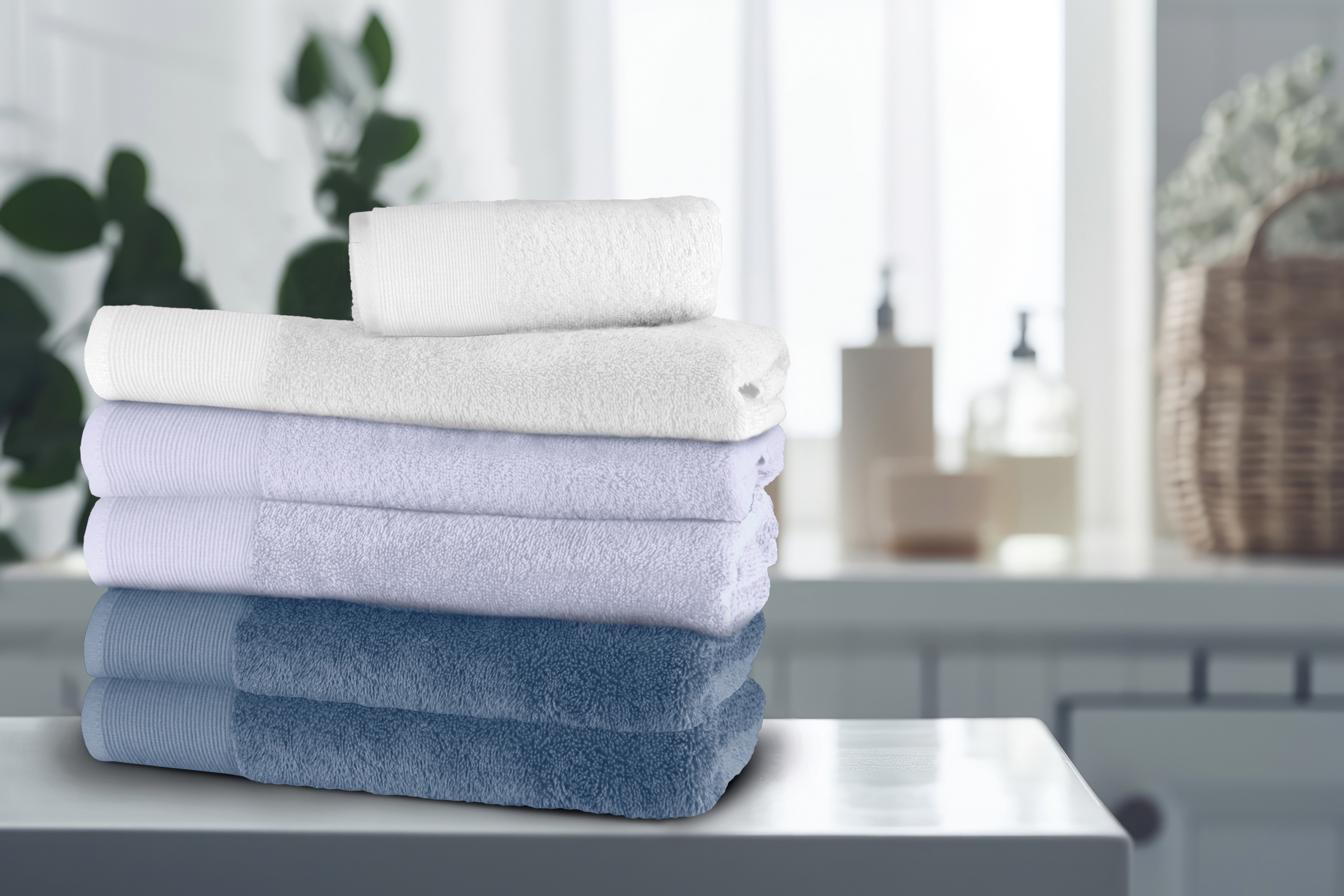Weiche, farblich abgestimmte Handtücher in Blau- und Weißtönen, gestapelt auf einem Tisch in einem modernen Badezimmer.