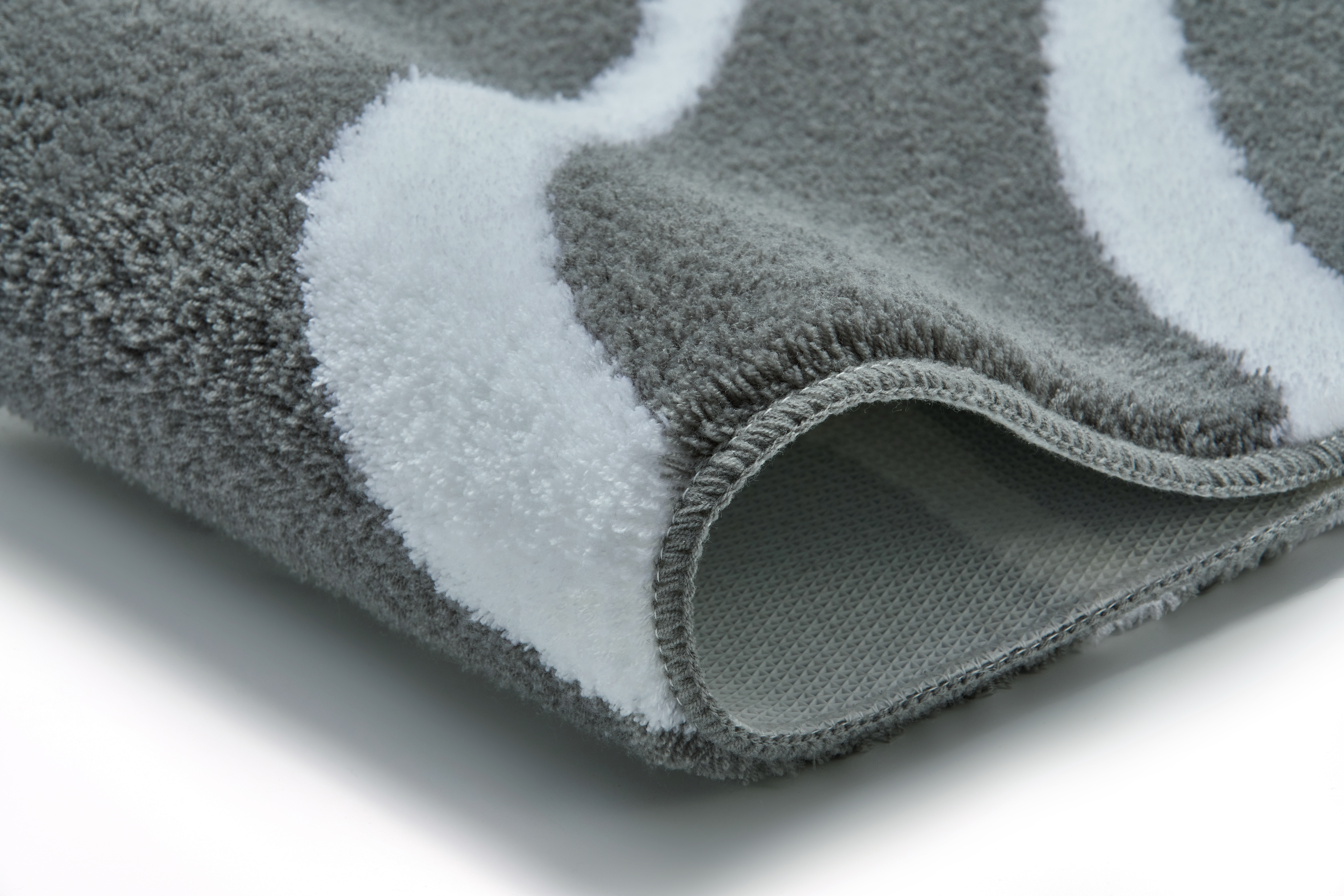 Grauer Badteppich mit weißen Wellenmustern, weiche Textur, Nahaufnahme der Kante, modernes Design.