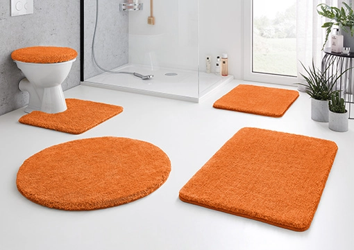 Orange Badematte-Set in modernem Badezimmer, bestehend aus WC-Deckelbezug, Duschvorleger, WC-Vorleger und zwei rechteckigen Matten.