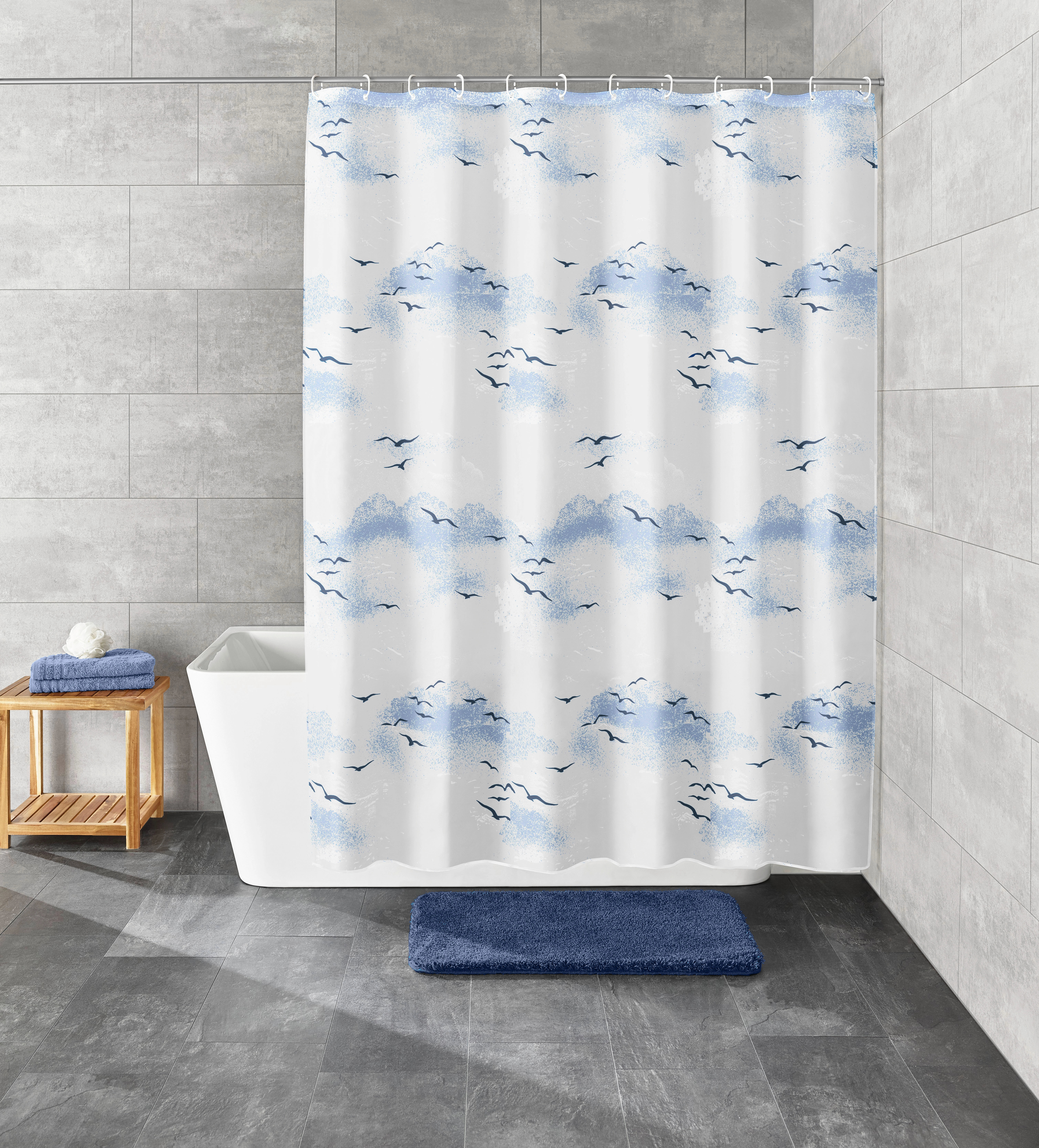 Duschvorhang mit blauem Wolken- und Vogelmotiv, dekoriert in einem modernen Badezimmer mit grauen Fliesen und Badewanne.
