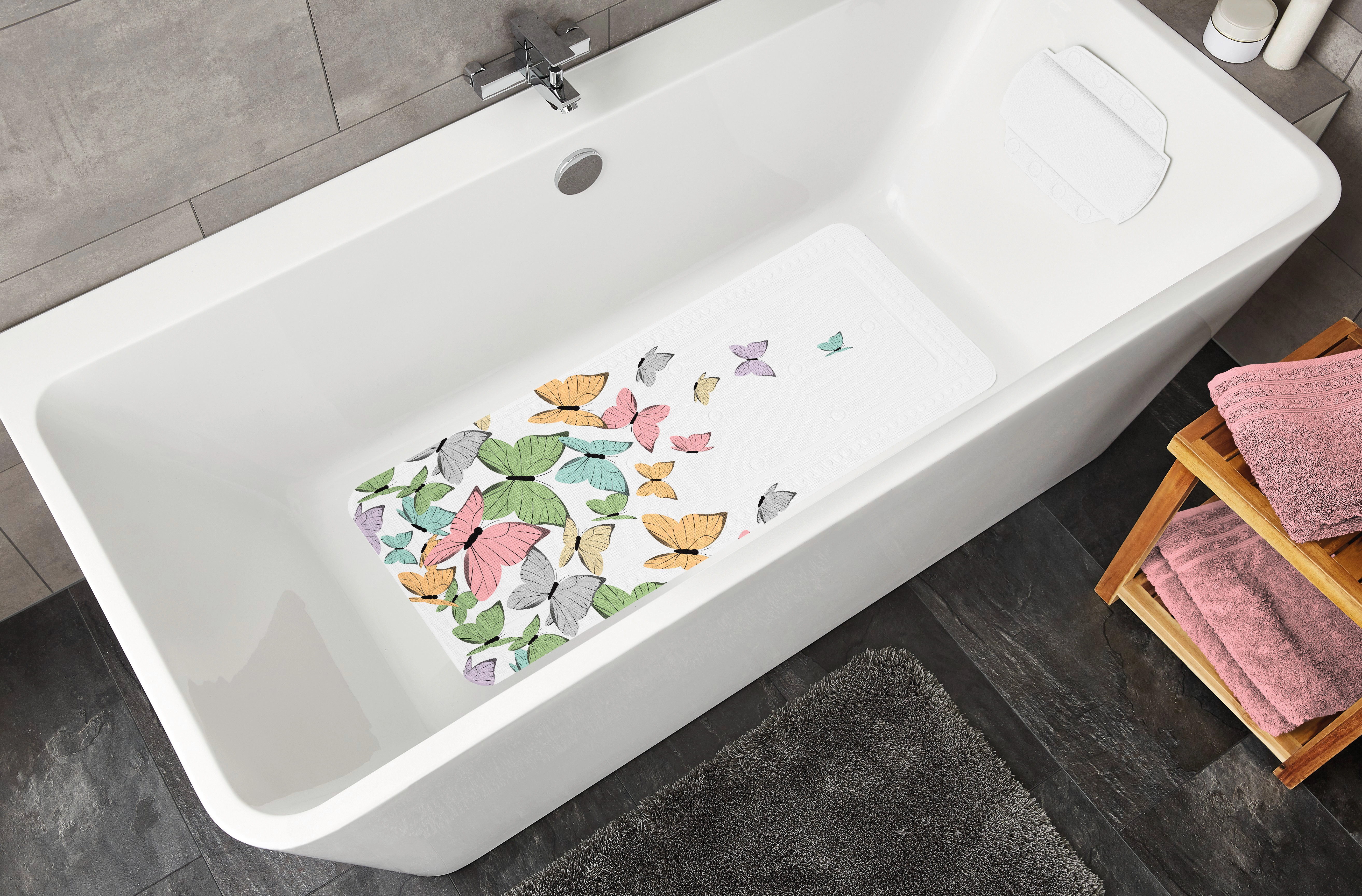 Bunte Schmetterlings-Badewannenmatte in weißer Badewanne, umgeben von grauen Fliesen und rosa Handtüchern.