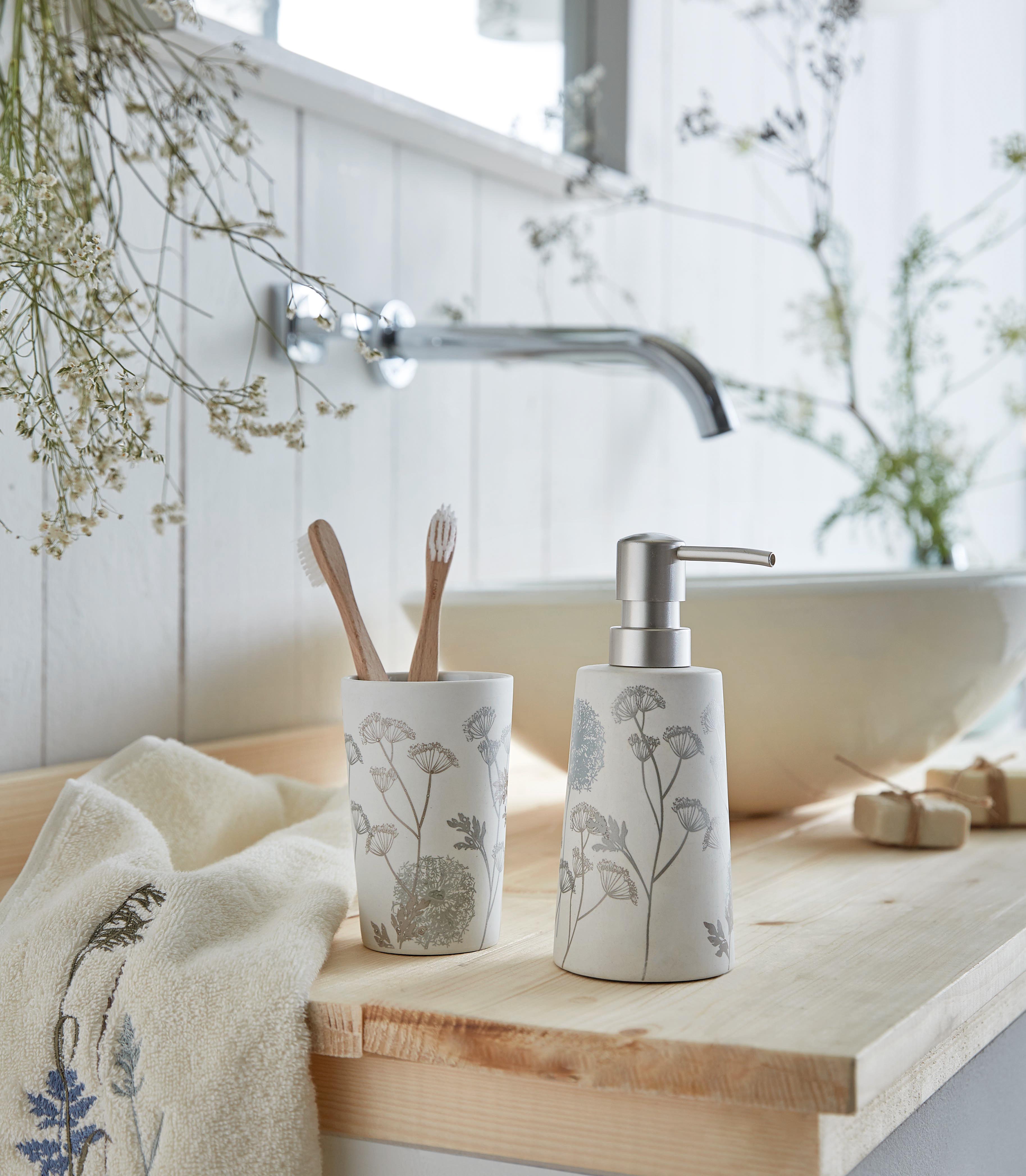 Seifenspender und Zahnputzbecher im floralen Design auf einem Holzwaschtisch, dekoriert mit Handtuch und Pflanzen.