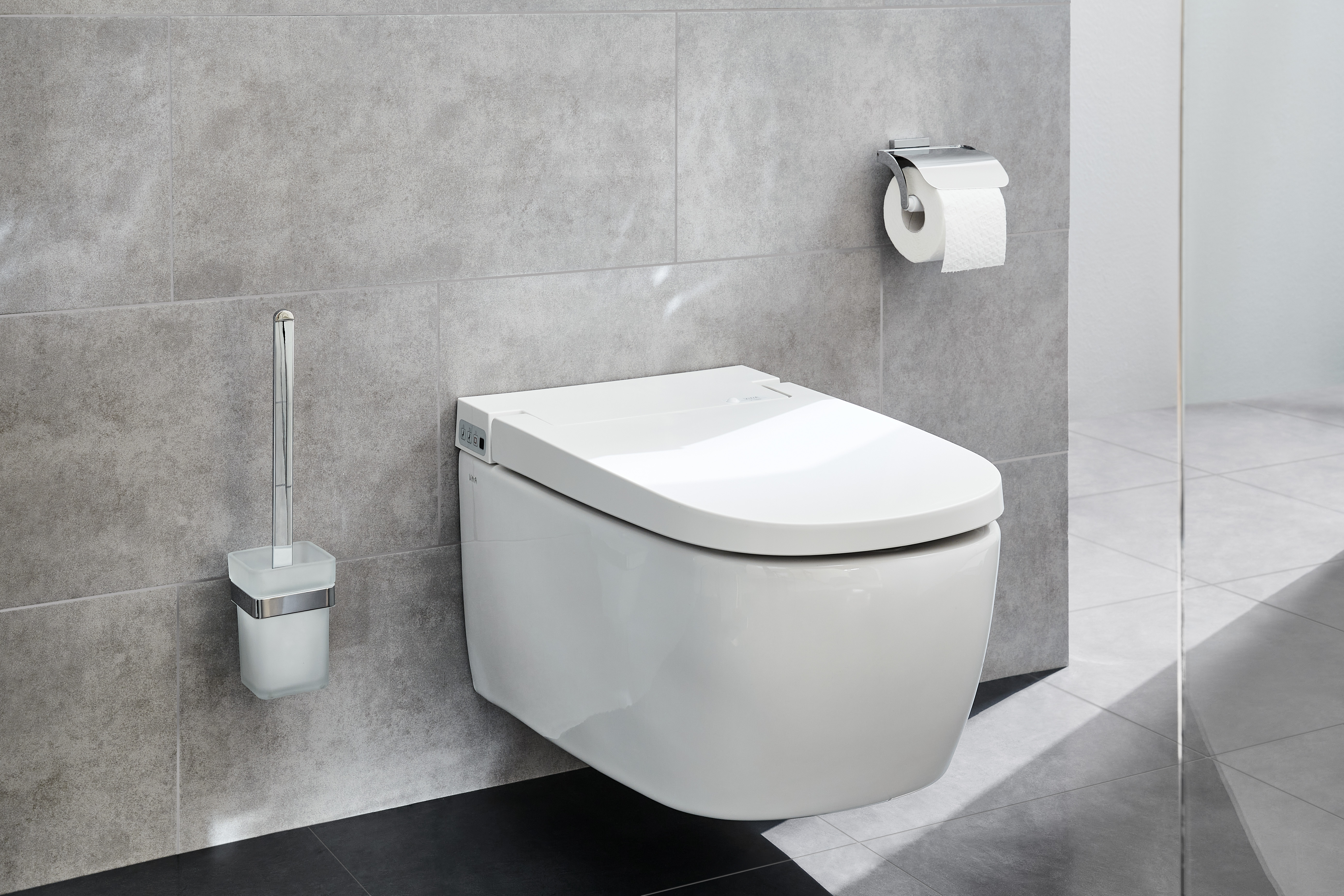 Modernes, wandhängendes WC mit integriertem Bidet, graue Fliesenwand, Toilettenpapierhalter und WC-Bürste in elegantem Design.
